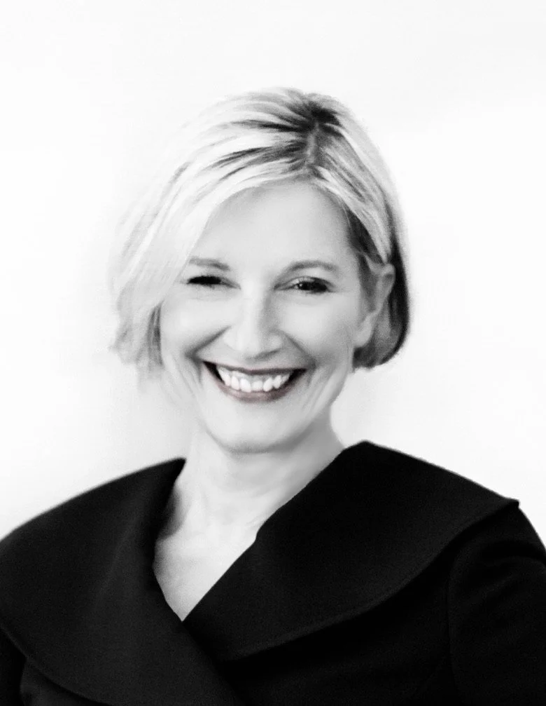 Black and white portrait of a woman with short blonde hair, winking and smiling, wearing a dark top.