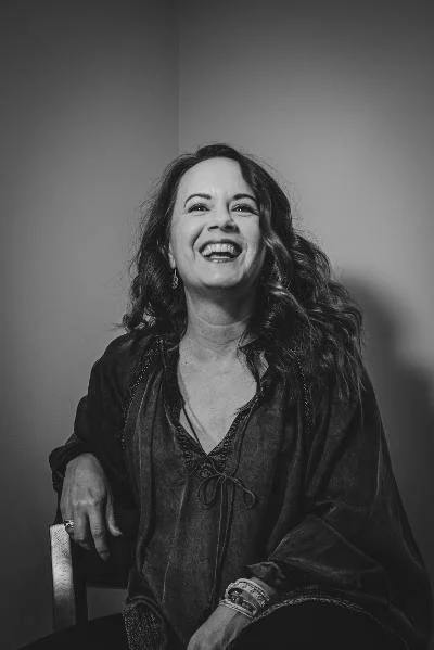 A woman with long curly hair smiling in a black and white photo.