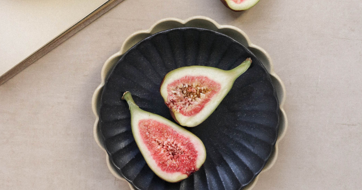 Two halves of a ripe fig fruit on a dark ceramic plate.