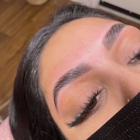 Close-up of a woman's face showing freshly shaped eyebrows and partial view of closed eyes, with long eyelashes, lying down.