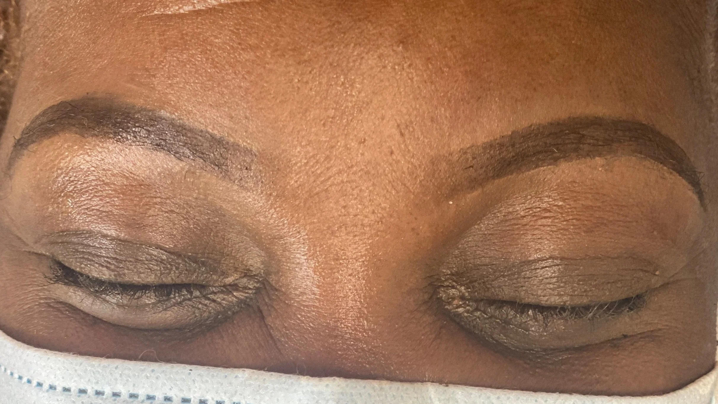 Close-up of closed eyes with well-groomed eyebrows and neutral eyeshadow, wearing a face mask.