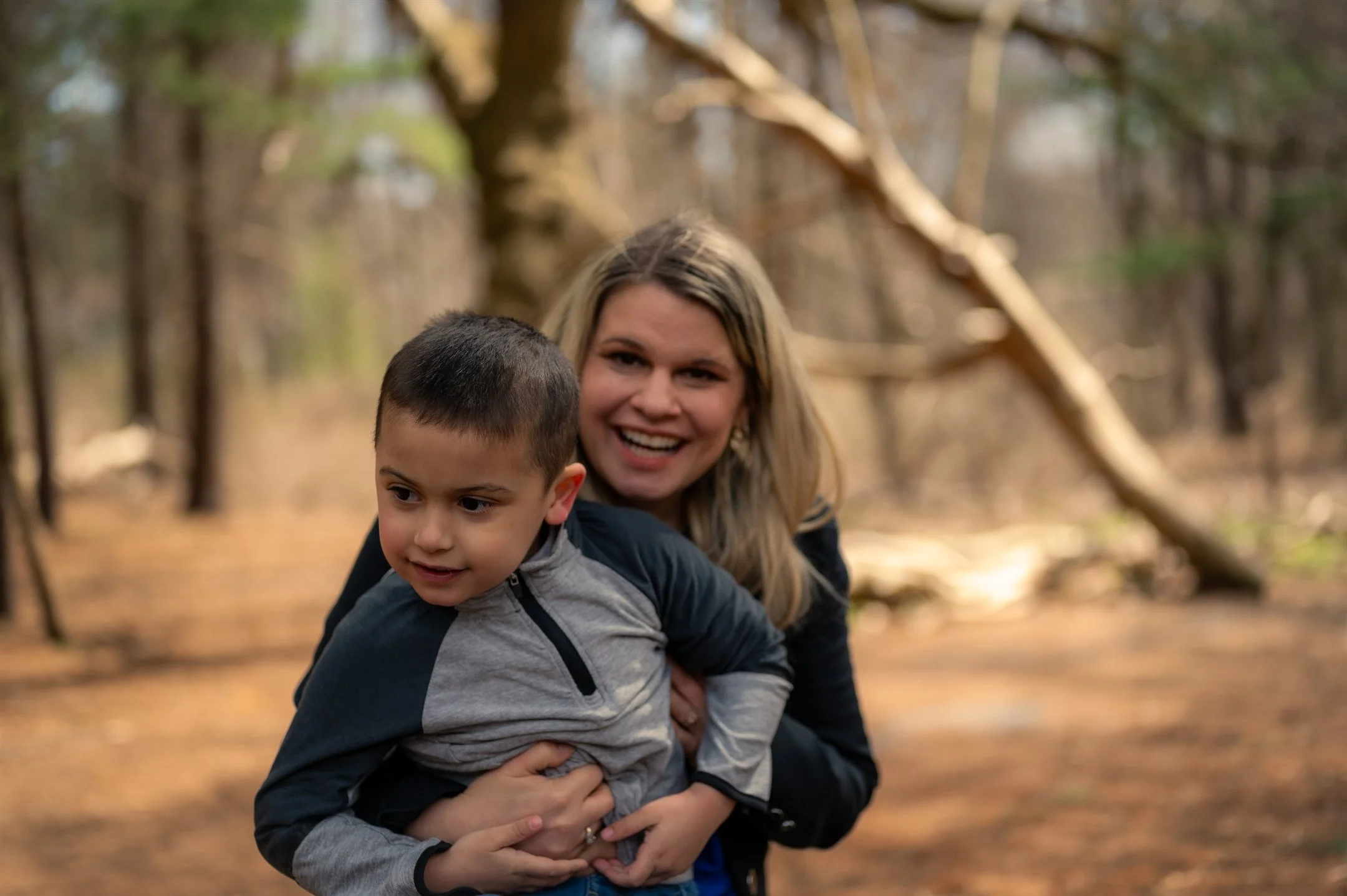 A woman and child smiling in a forest setting.