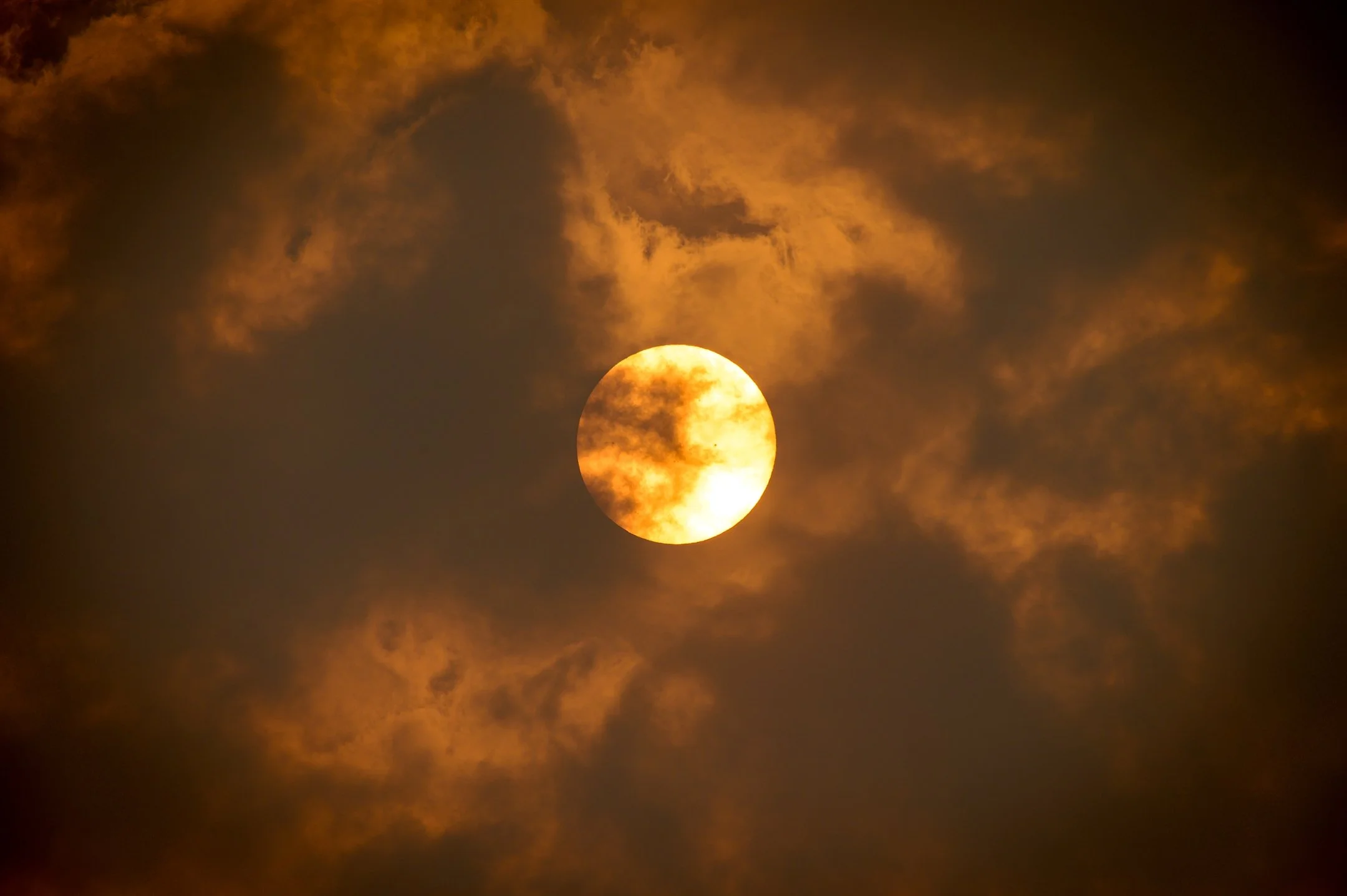 Bright sun behind dark clouds with an overcast sky.