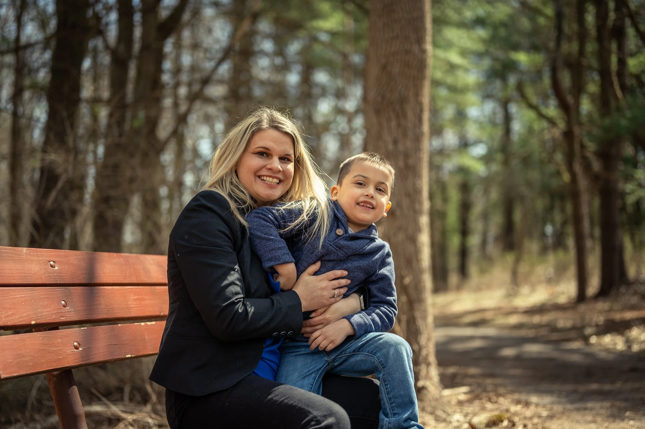 Smiling woman holding a child on a park bench in a forest.