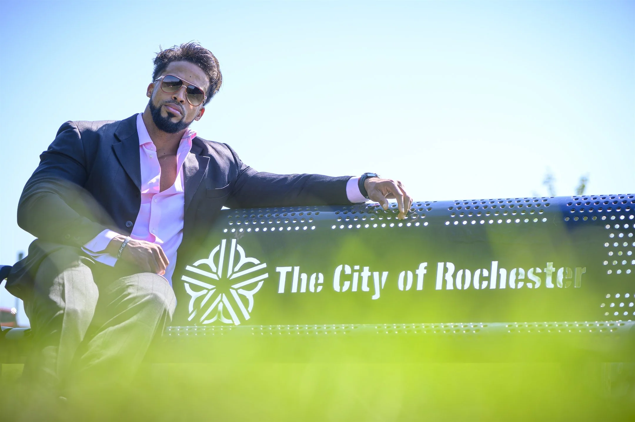 Man in sunglasses and suit sitting on Rochester city bench