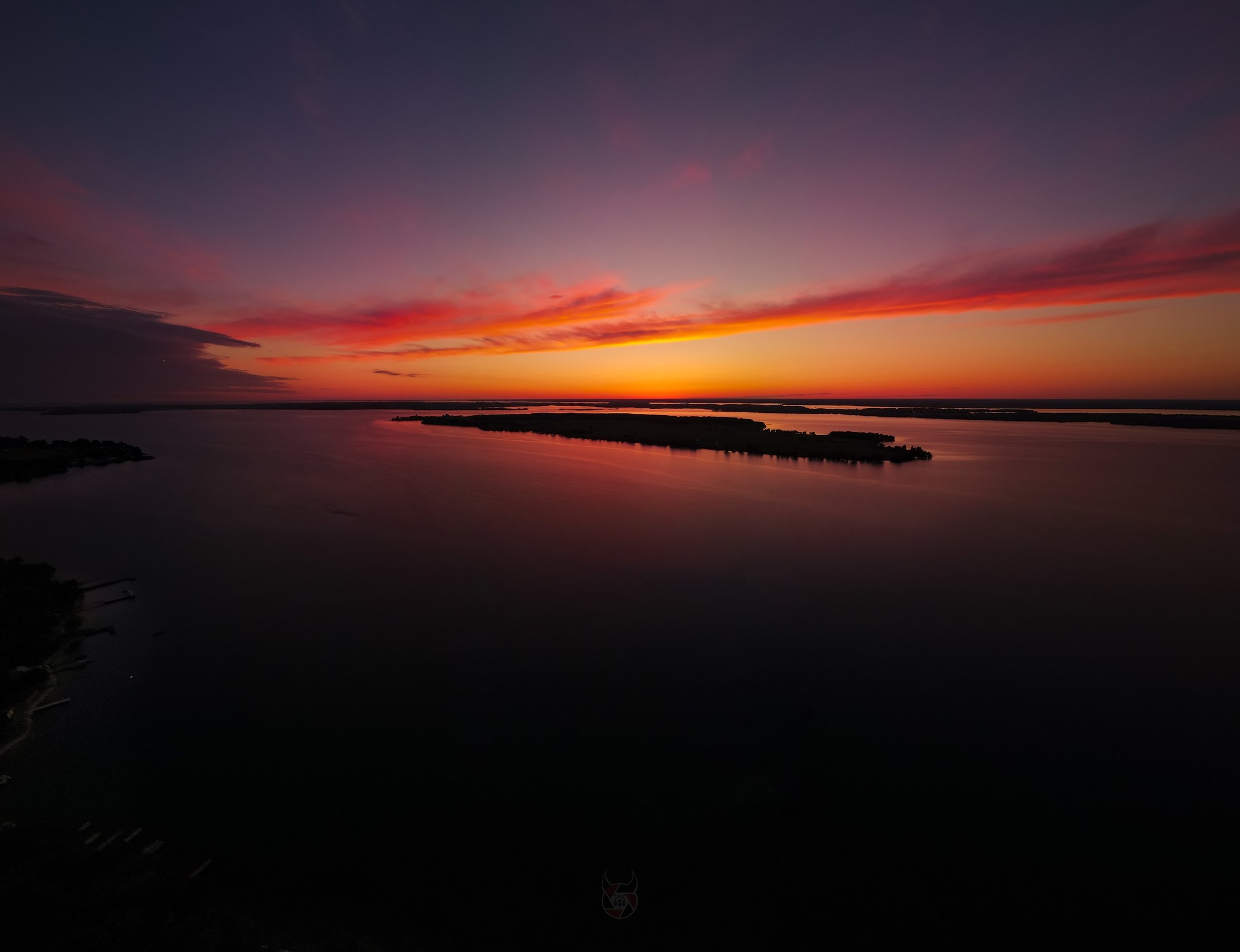 Silhouette of an island during a vibrant sunset with orange and pink hues over a calm body of water.