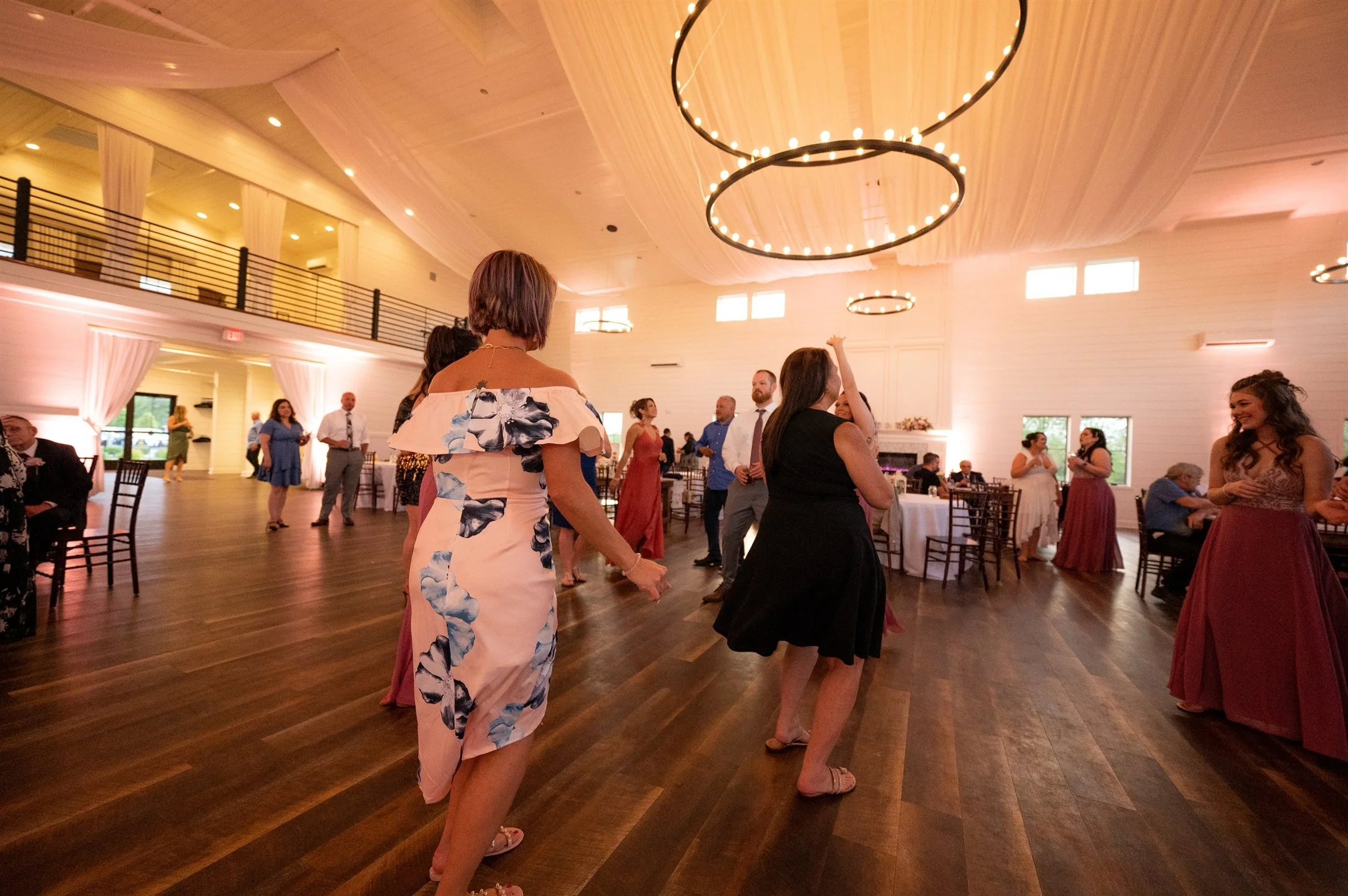 People dancing at an indoor event, possibly a wedding reception, with elegant decor and lighting.