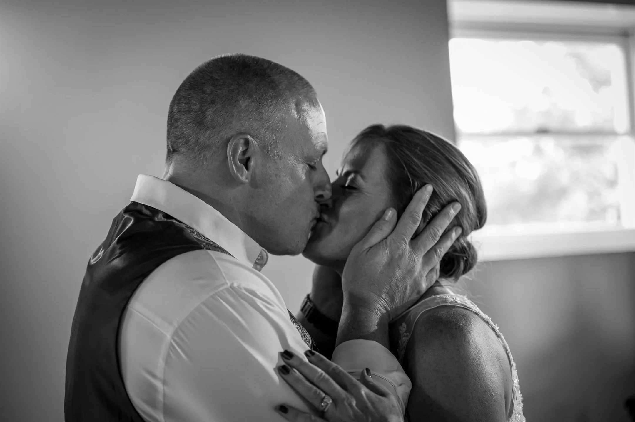 Black and white photo of a couple kissing intimately indoors.