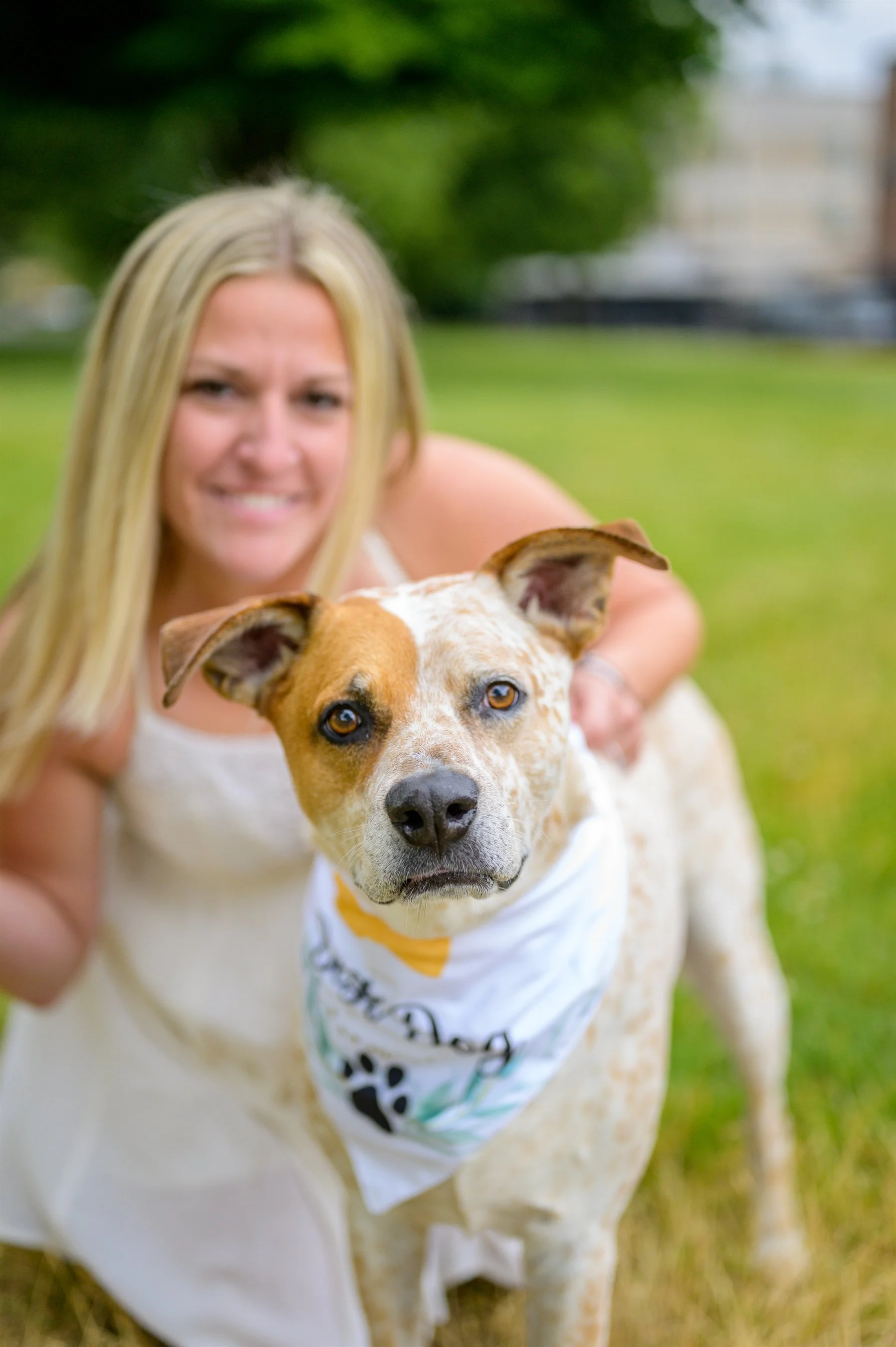 Woman with a dog wearing a bandana, outdoors on grass.