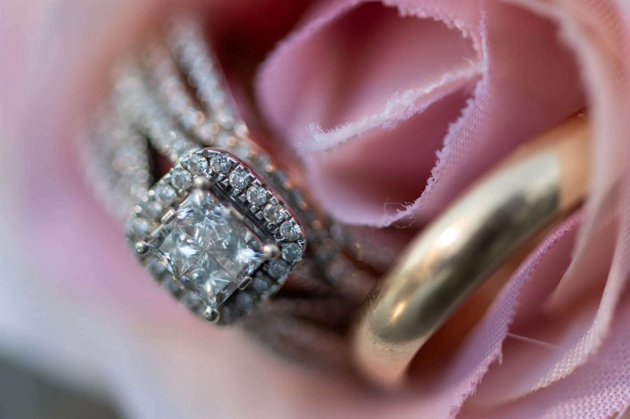 Close-up of a diamond engagement ring and wedding band nestled in a pink flower.