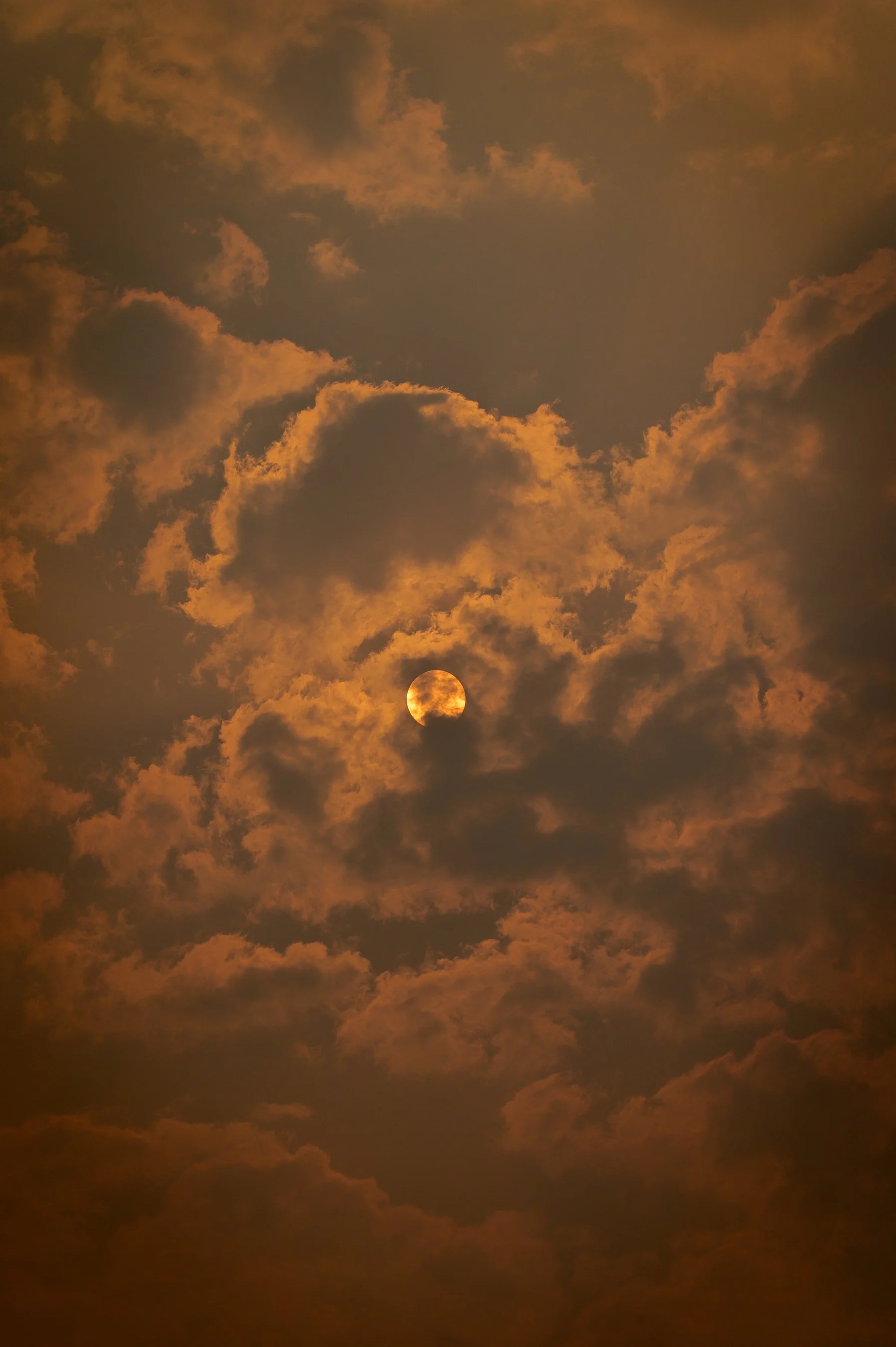 Sunset sky with clouds partially covering the sun, creating a dramatic, golden orange atmosphere.