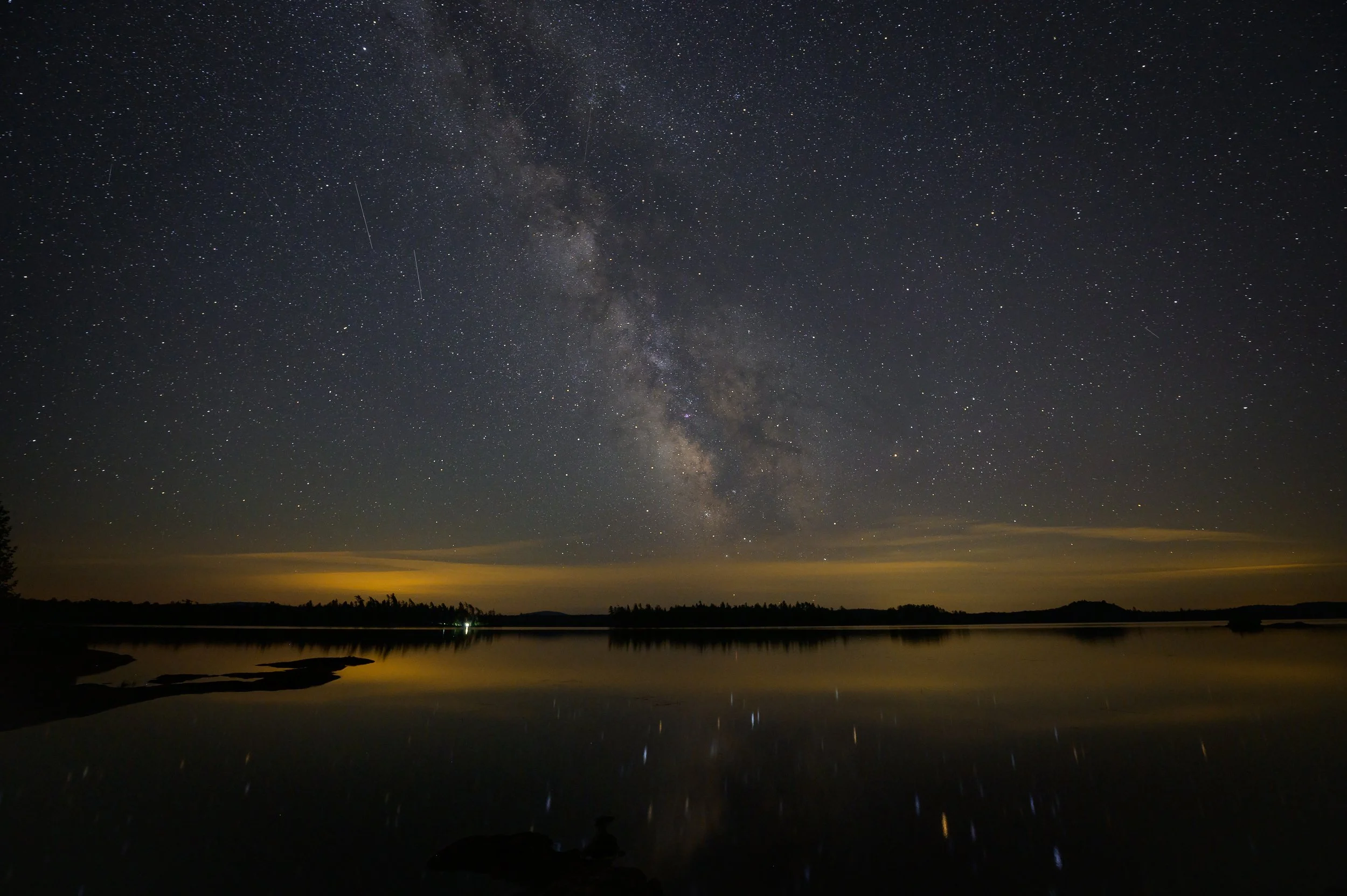 Night sky with Milky Way over a lake, reflecting stars on the water surface.