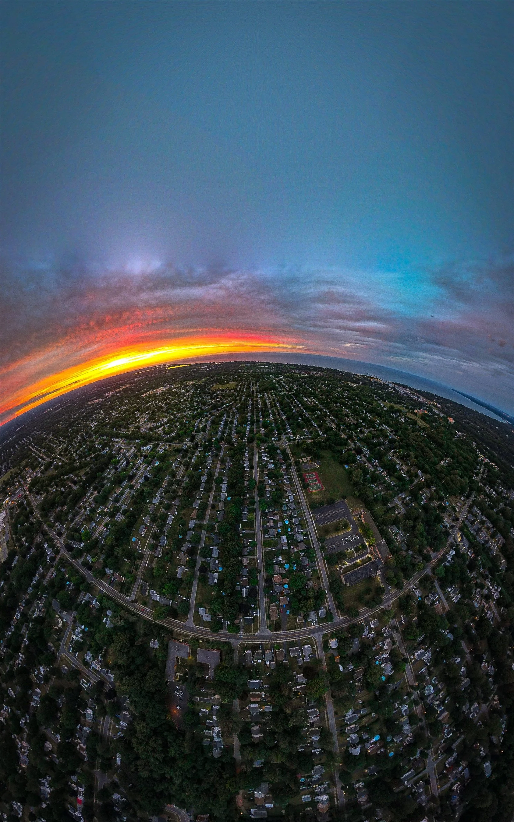 Aerial view of suburban neighborhood at sunset with curved horizon and colorful sky.