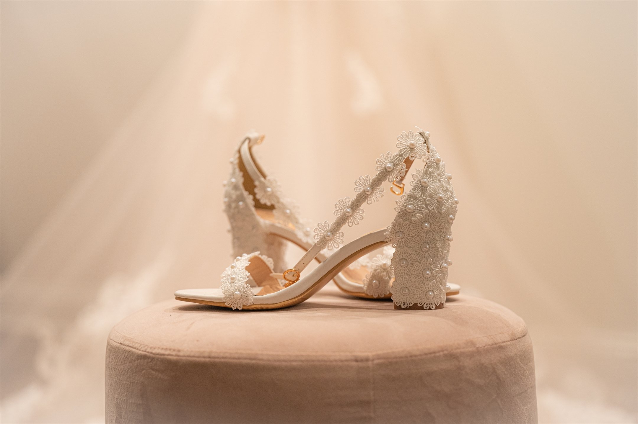 White lace bridal heels with pearl embellishments on a round stool.