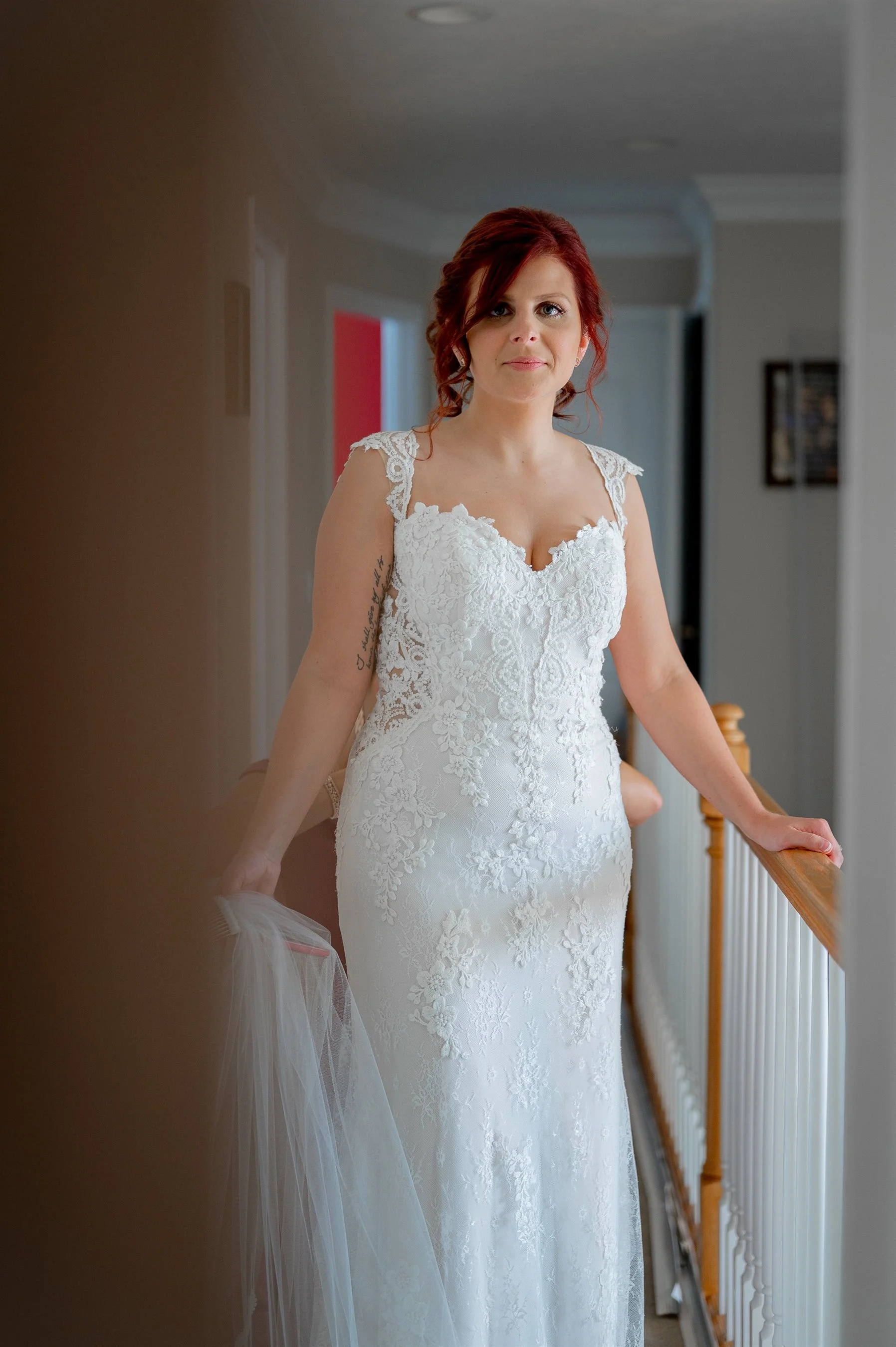Bride in a lace wedding dress with red hair, standing in a hallway.