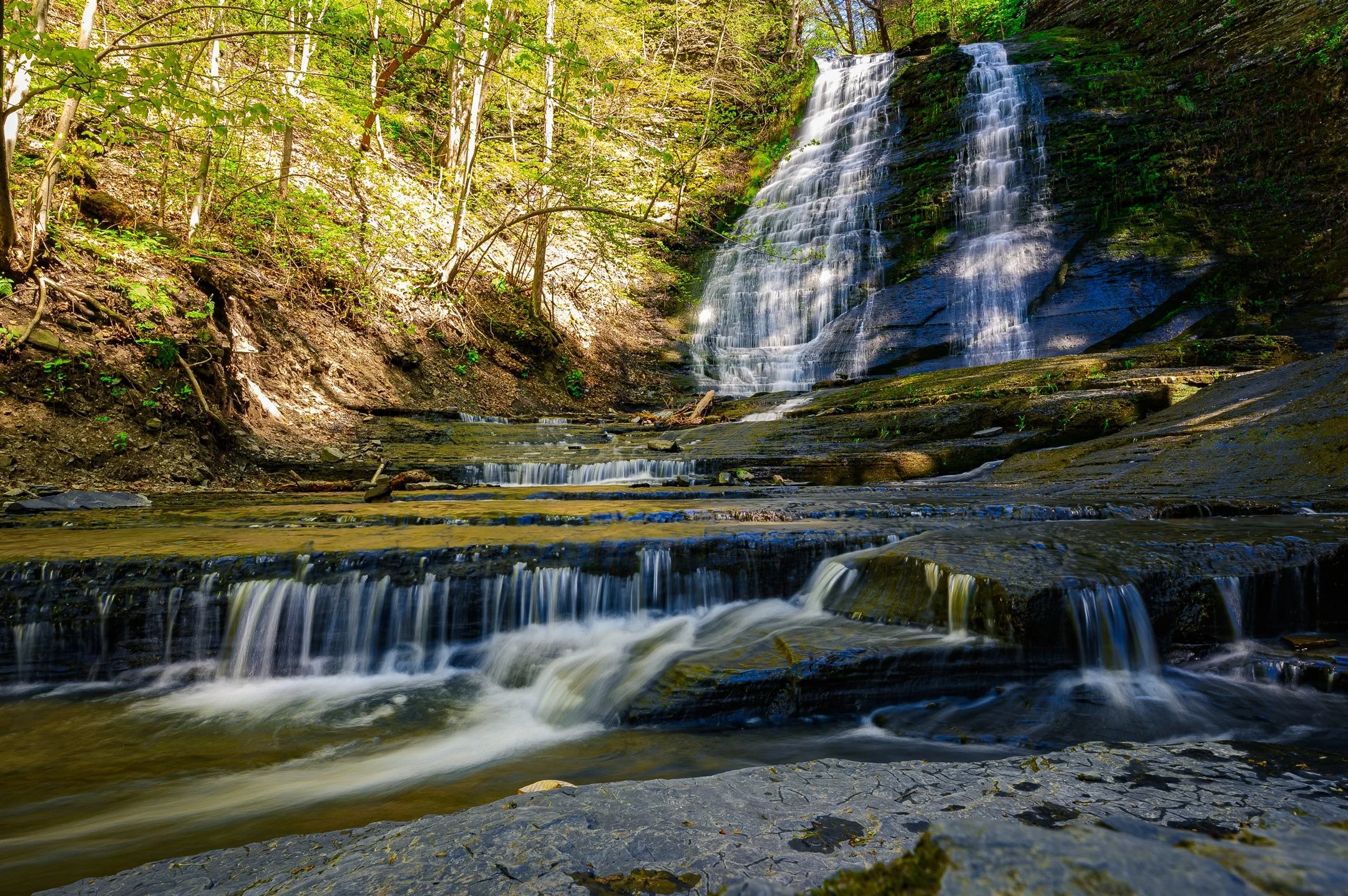 Beautiful multi-tiered waterfall cascading over rocks in a lush green forest.