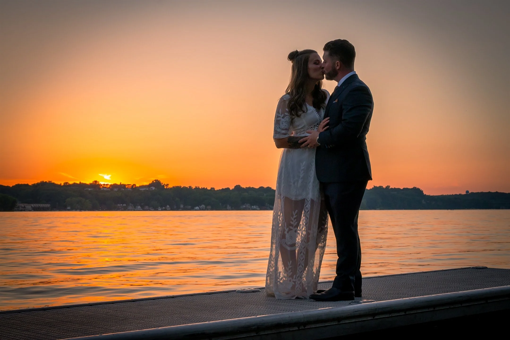 Couple kissing on a lakeside dock at sunset.