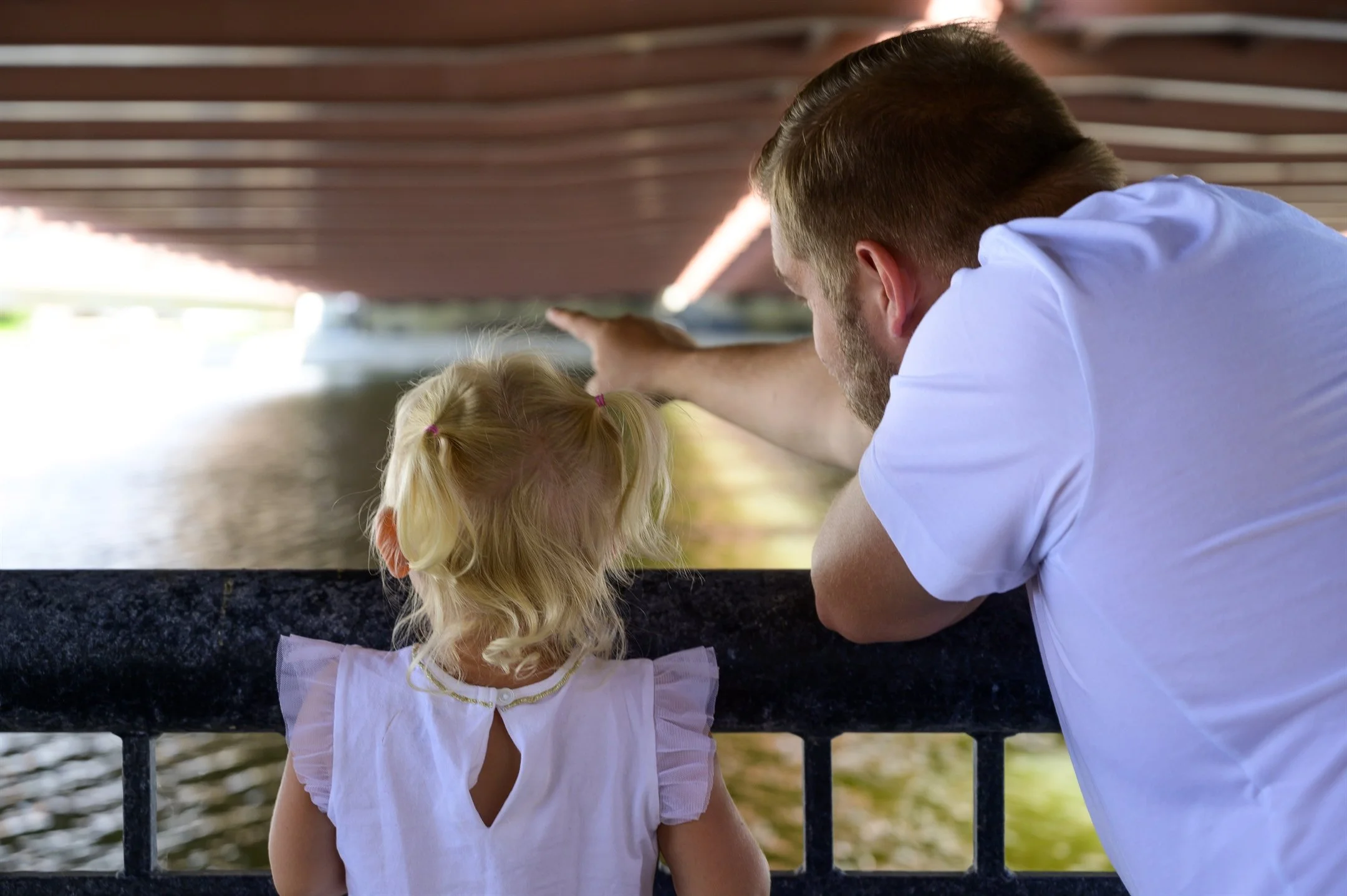 A man and a young girl look out from a bridge, pointing towards the water below.