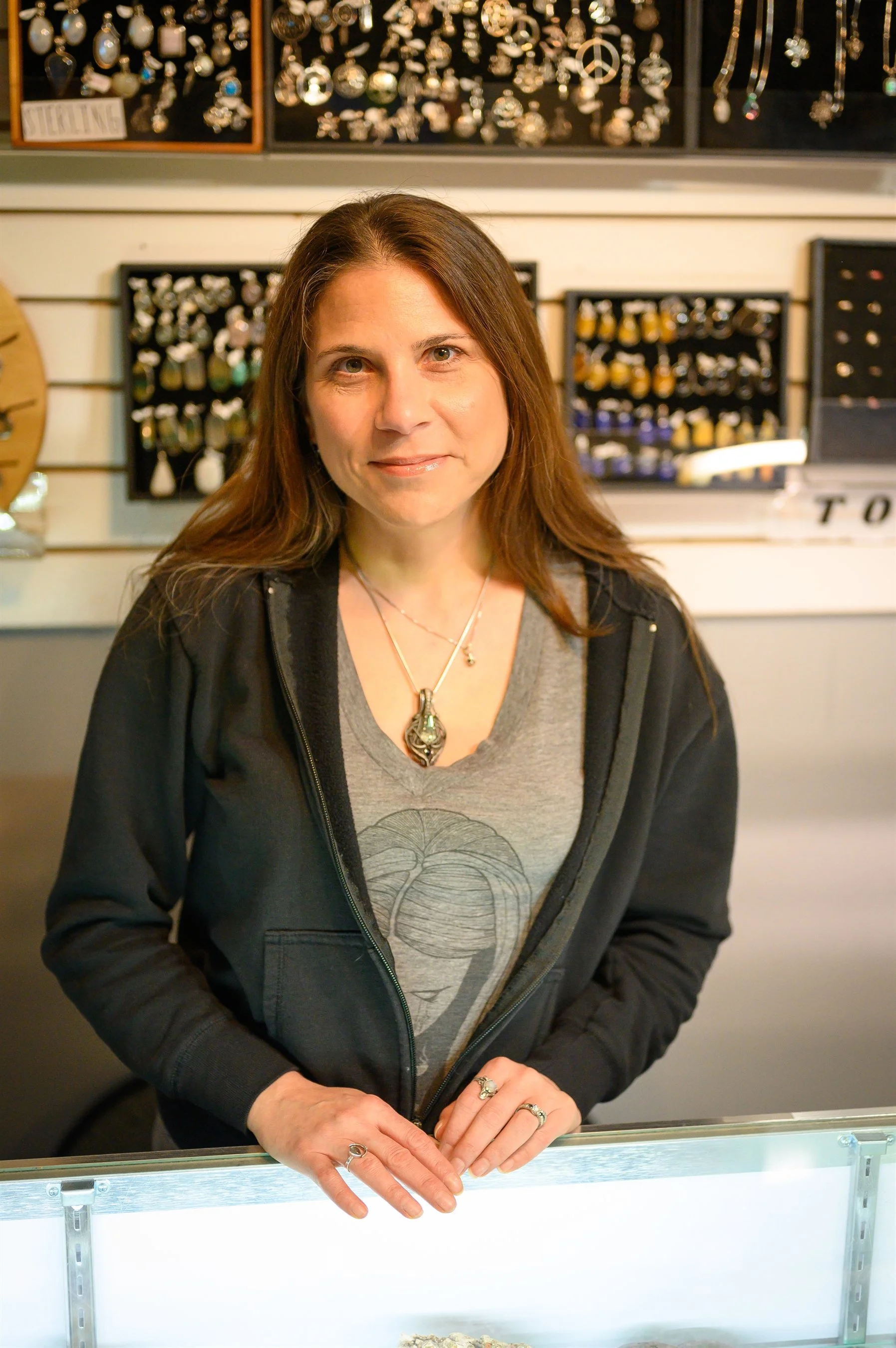 Person standing in front of a jewelry display wearing a gray shirt with a design and several rings.