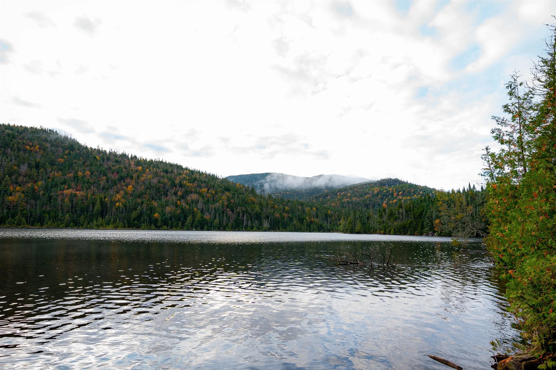Serene lake with surrounding forested hills and cloudy sky in autumn.