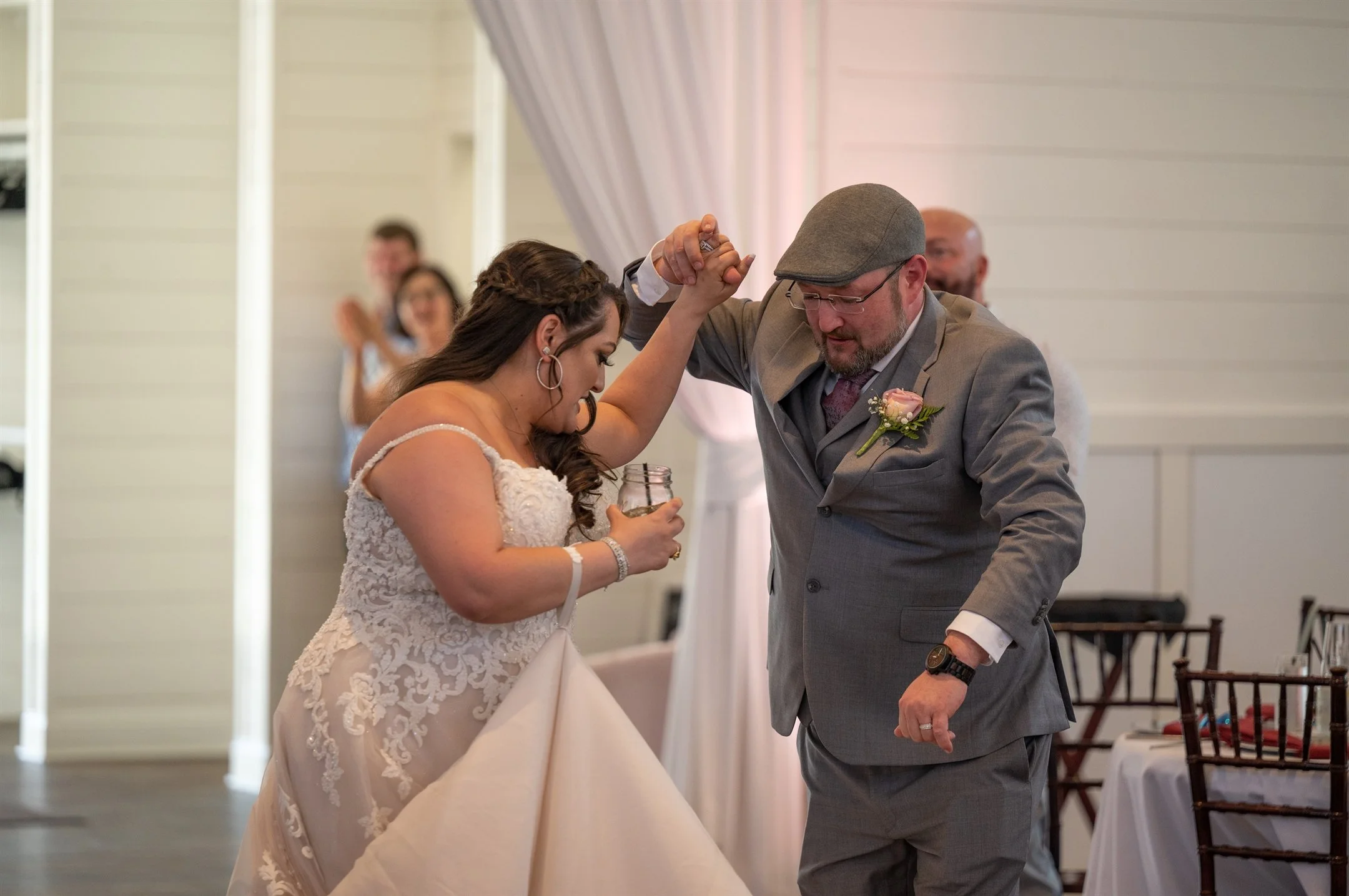 A bride and groom dancing at their wedding reception, with guests clapping in the background.