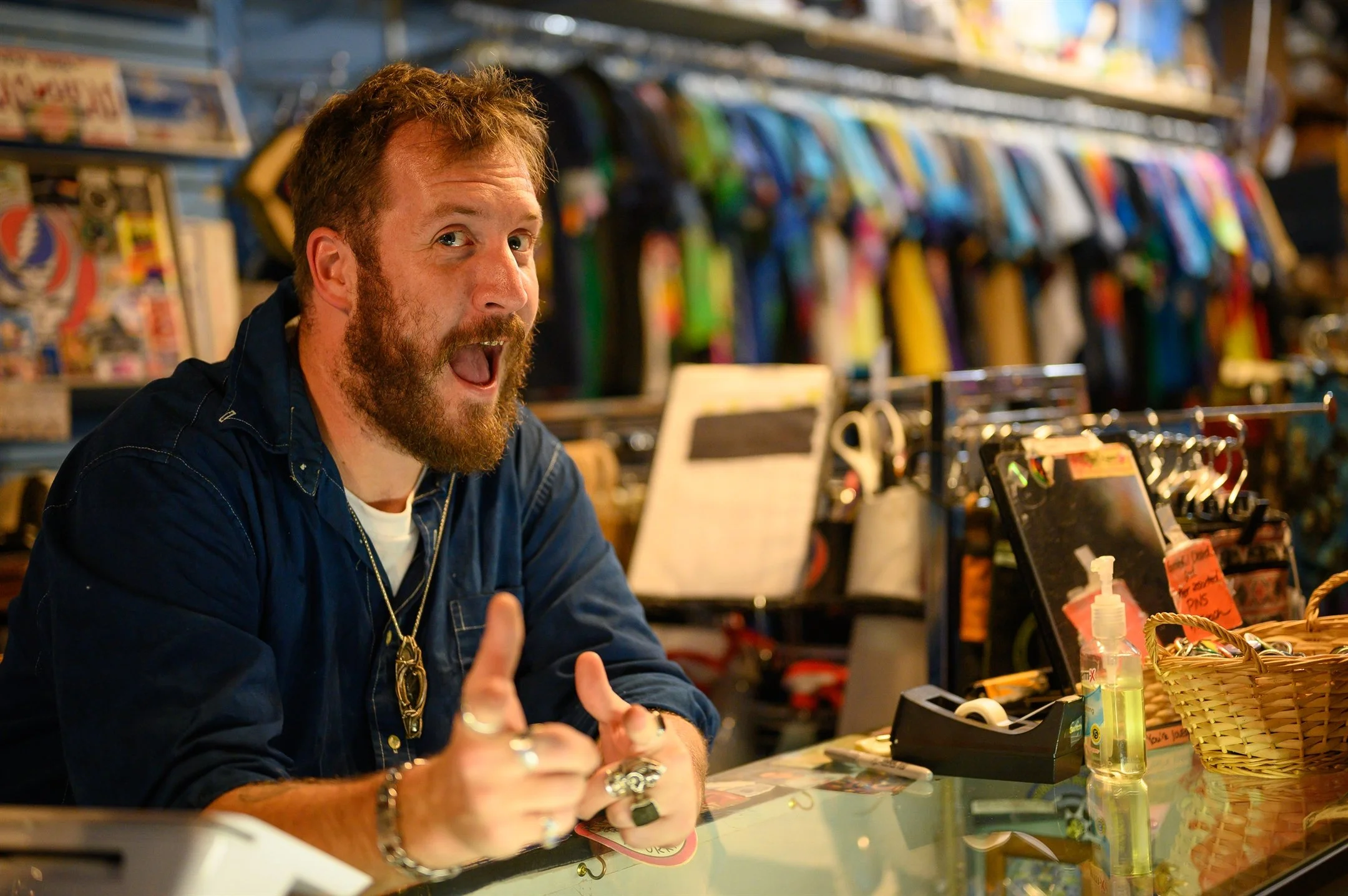 Man with a beard at a store counter with colorful clothes in the background