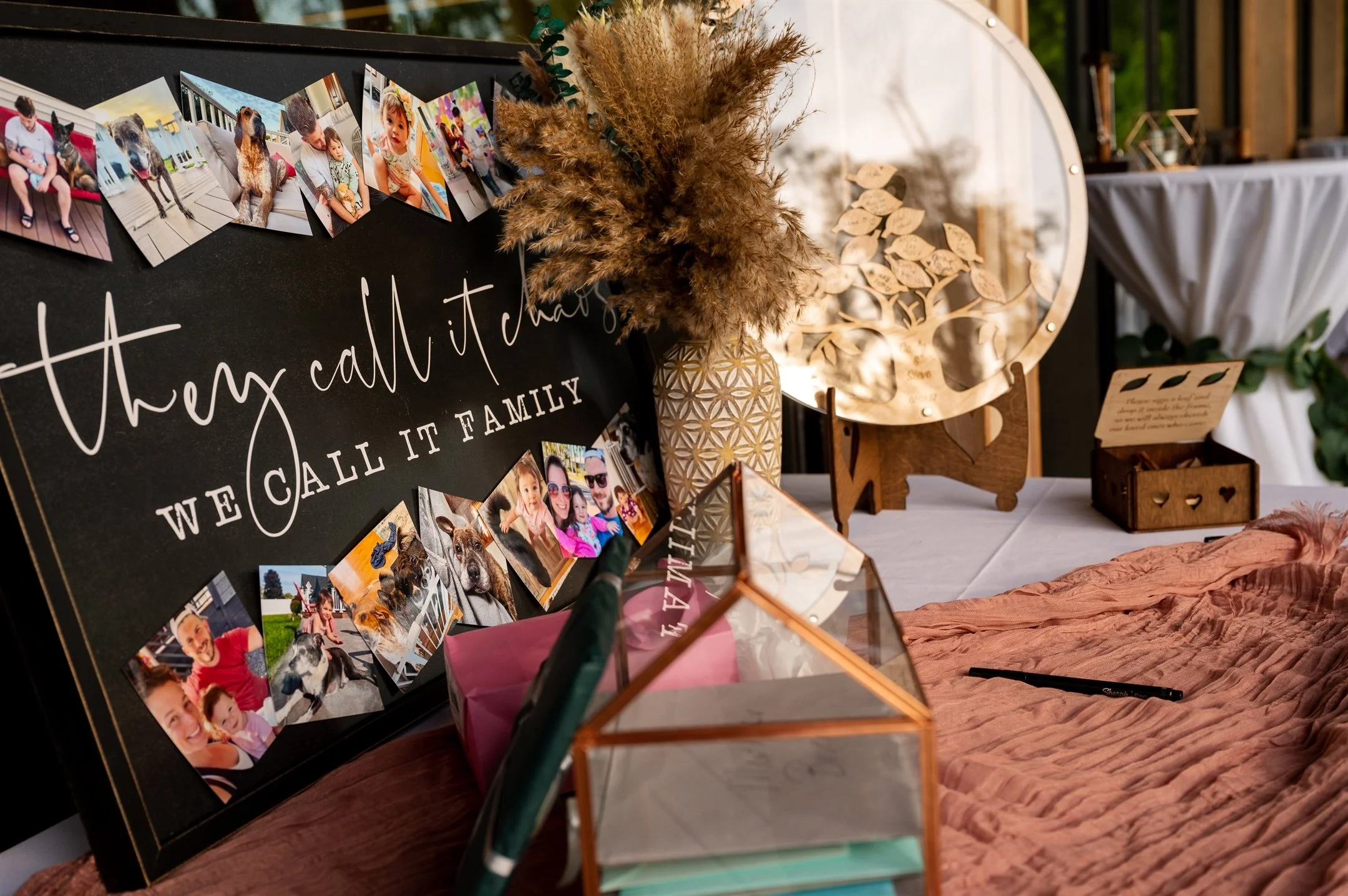 Display of a family-themed collage with photos and decorative elements, including pampas grass in a vase, a wooden ornament, and a glass box on a table.