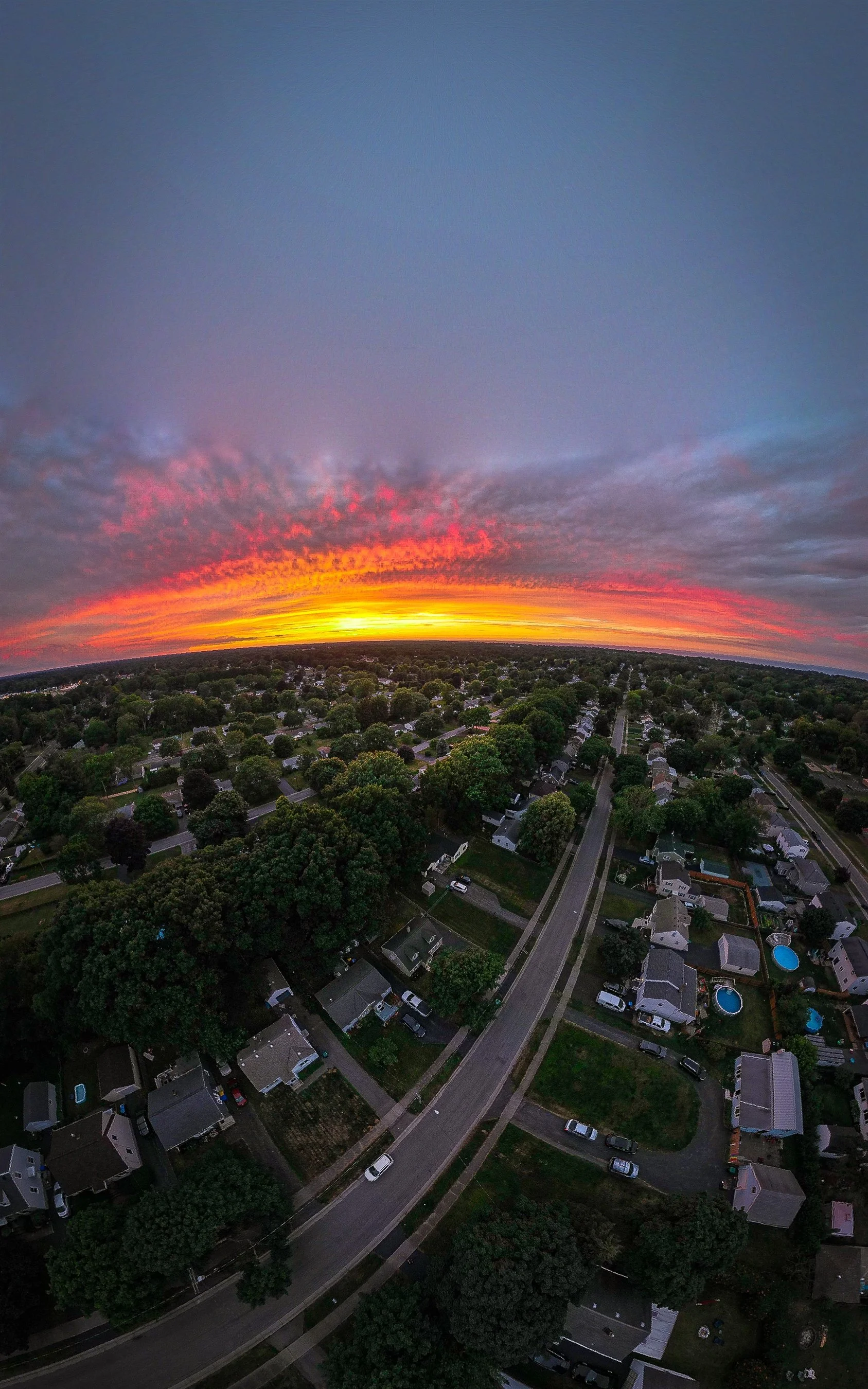 Aerial view of a suburban neighborhood at sunset with a vibrant, colorful sky and scattered clouds.