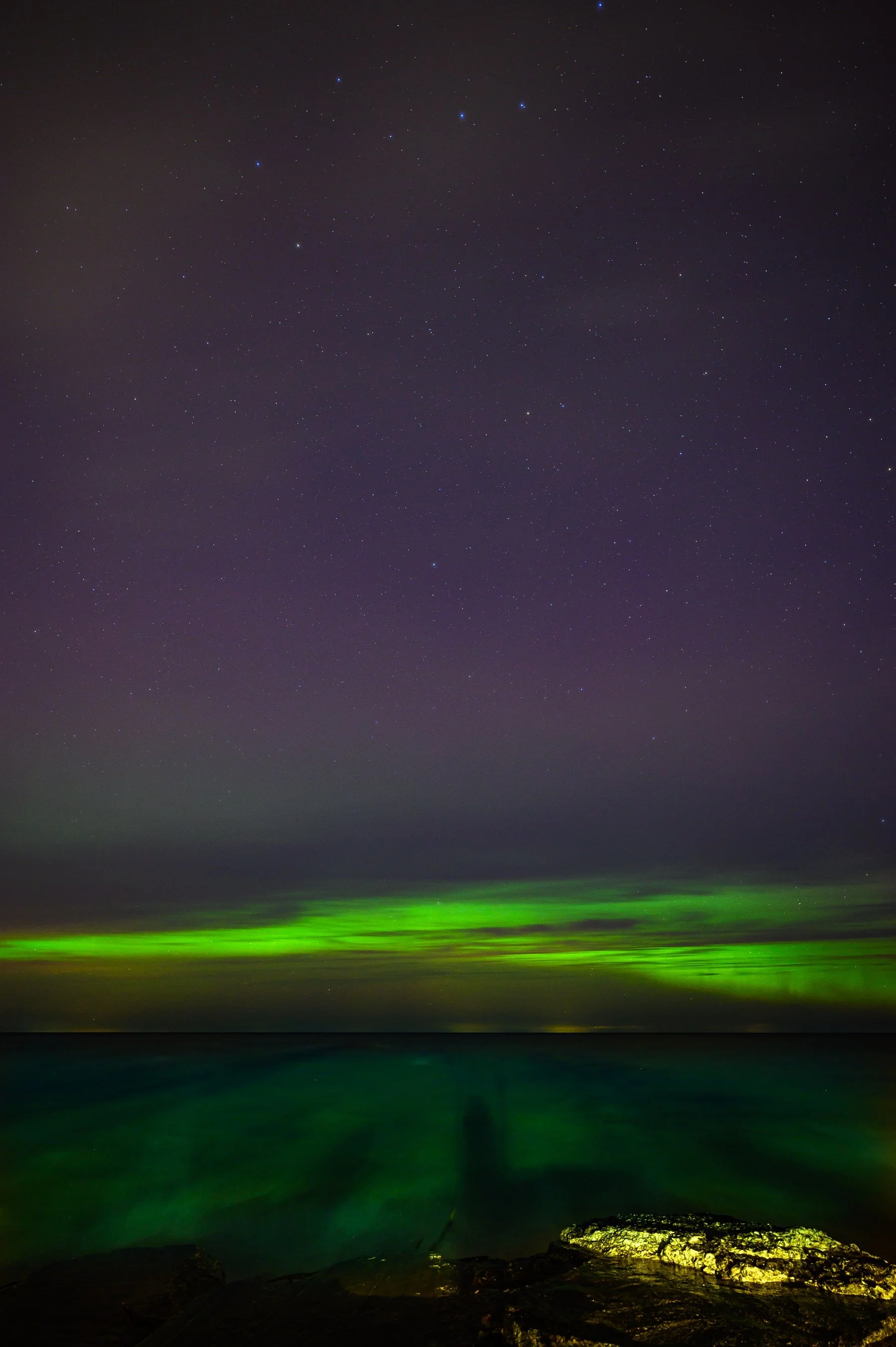 Night sky with aurora borealis over water and rocks