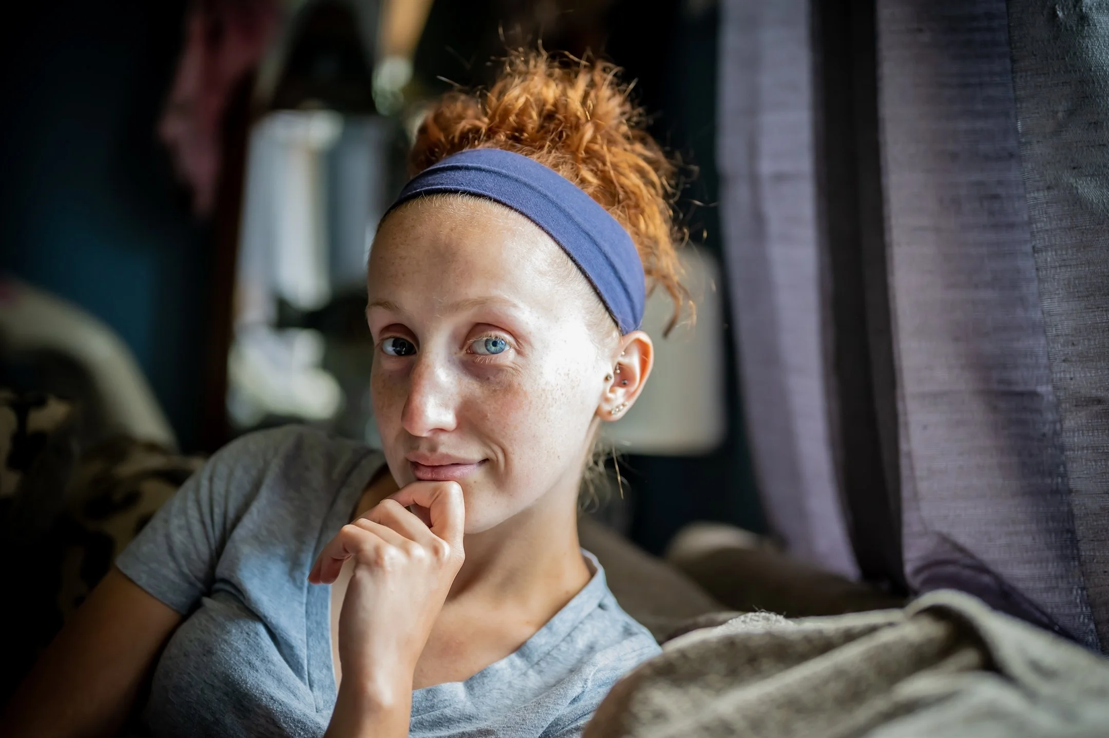 Smiling woman with curly red hair and headband, sitting indoors.