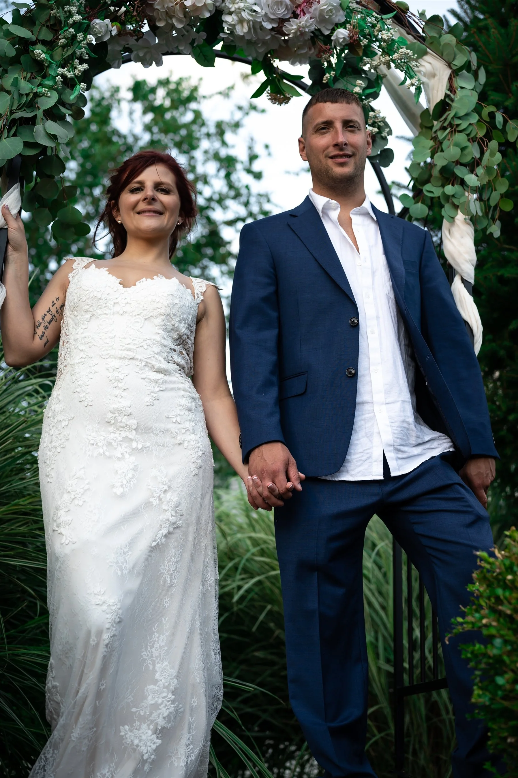 Bride and groom holding hands under floral arch, outdoor wedding ceremony.