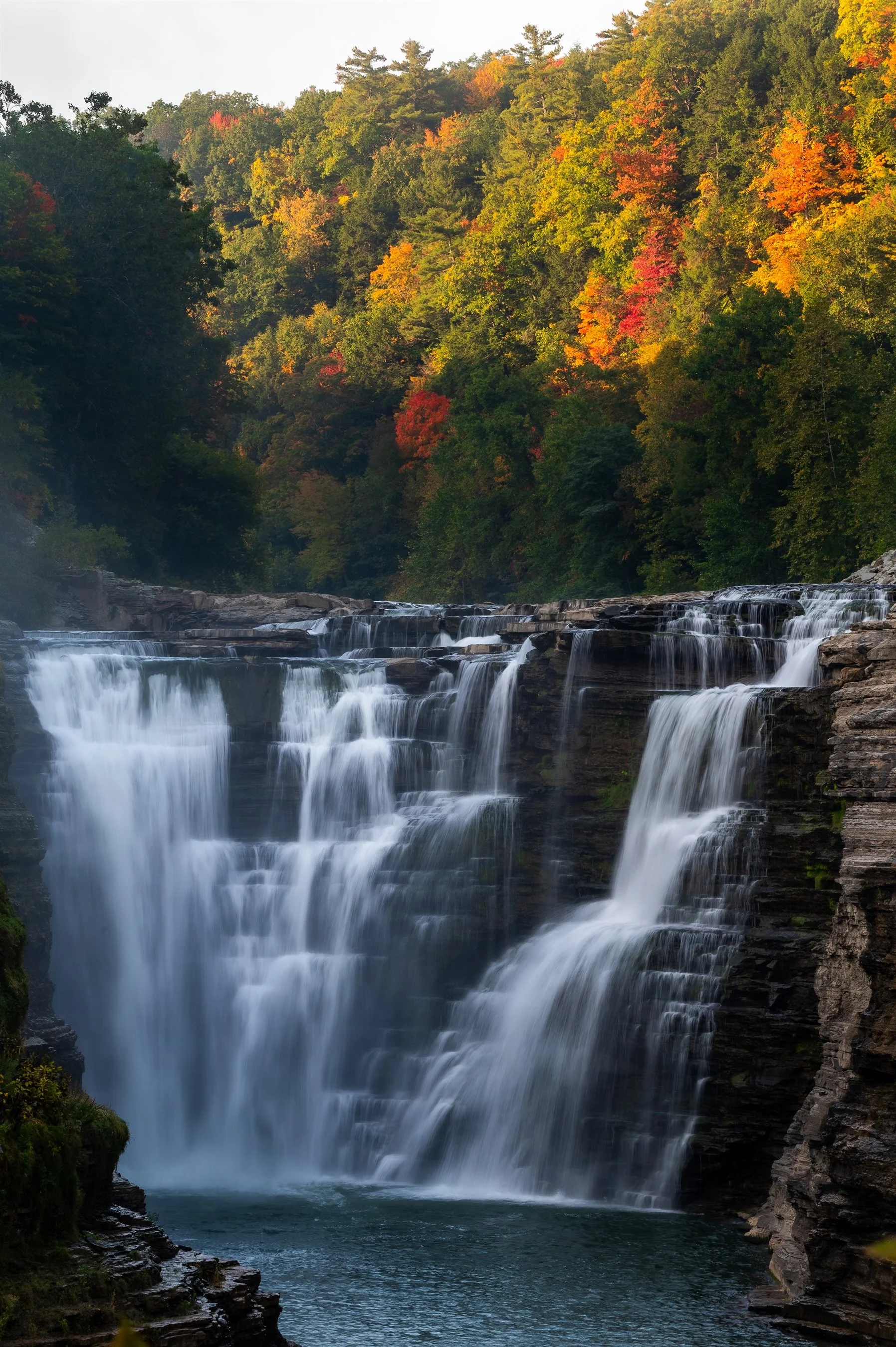 Waterfall cascading over rocks surrounded by autumnal forest with colorful foliage.