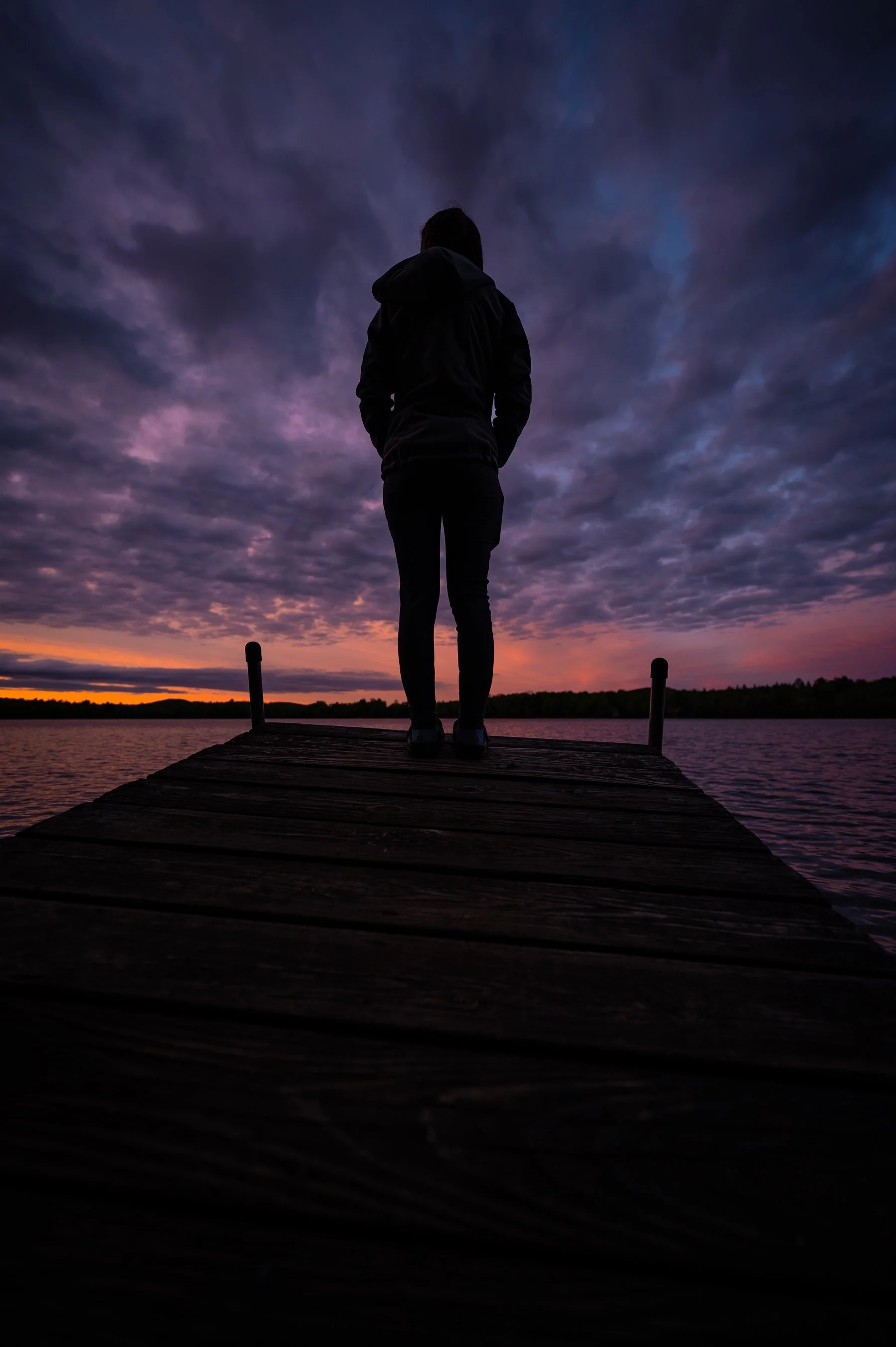 Silhouette of a person standing on a wooden dock at sunset with a dramatic sky.