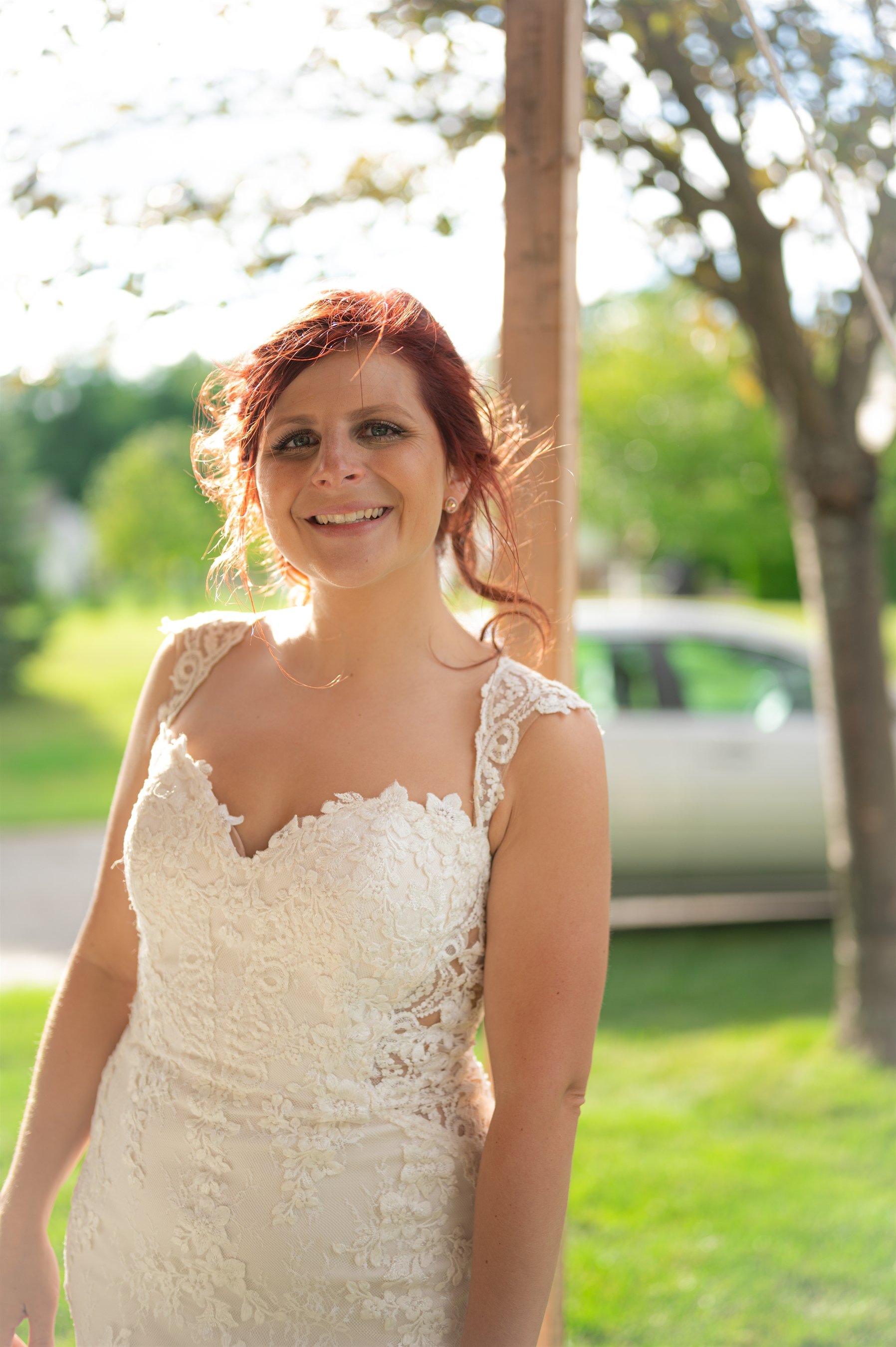 Woman in a wedding dress smiling outdoors, with trees and grass in the background.