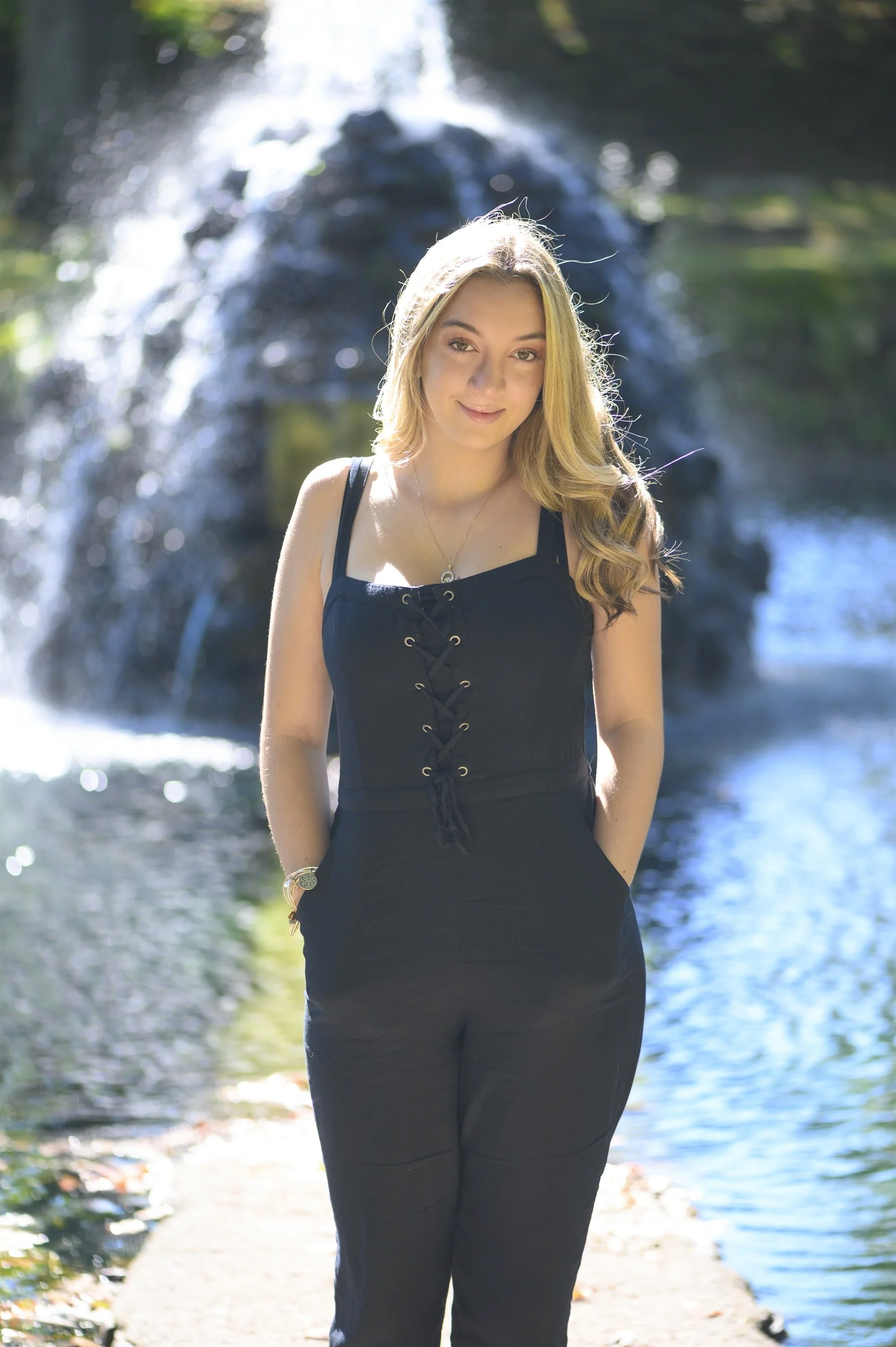 Woman in black outfit standing by a fountain waterfall in a park.