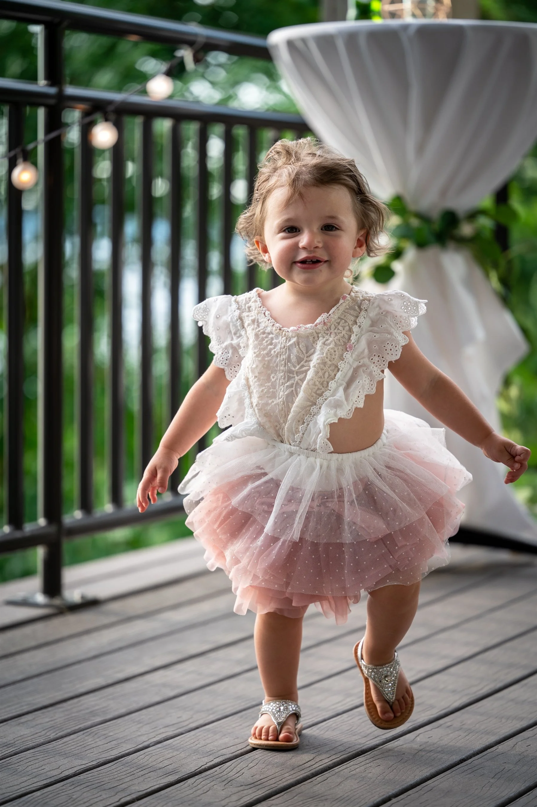Young child in a white and pink tutu dress with ruffled sleeves, running on a wooden deck.