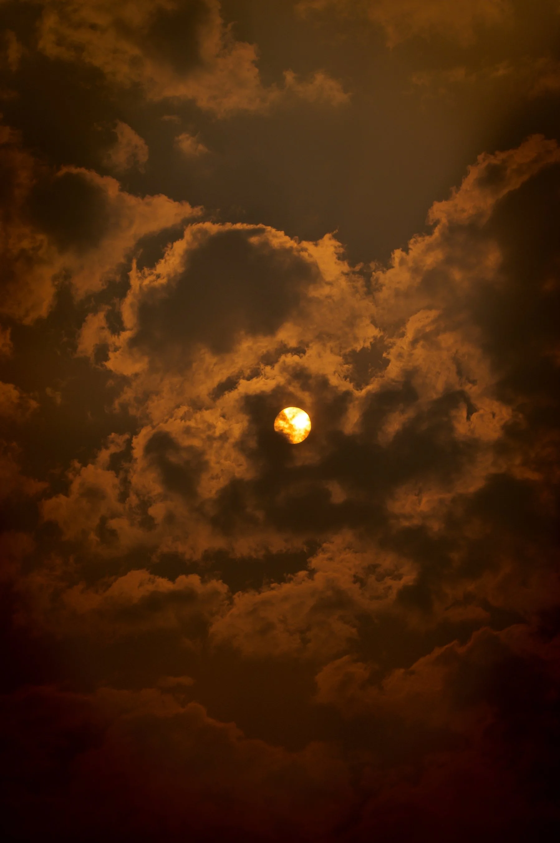 Sun shining through dramatic clouds with a reddish hue, creating a moody atmosphere.