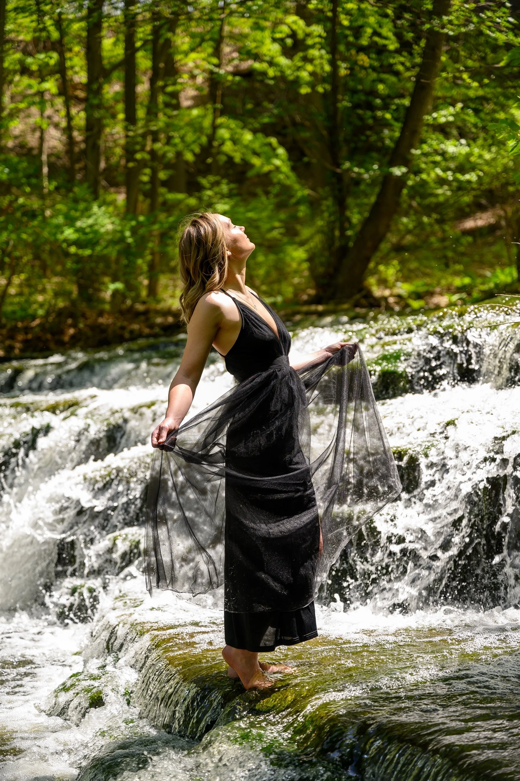 Woman in a black dress standing on a rock in a waterfall