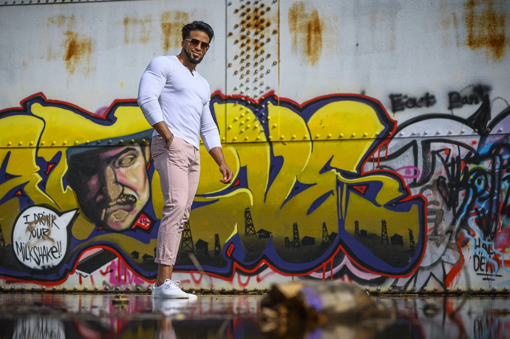 Man in white shirt and pink pants standing in front of colorful graffiti mural.