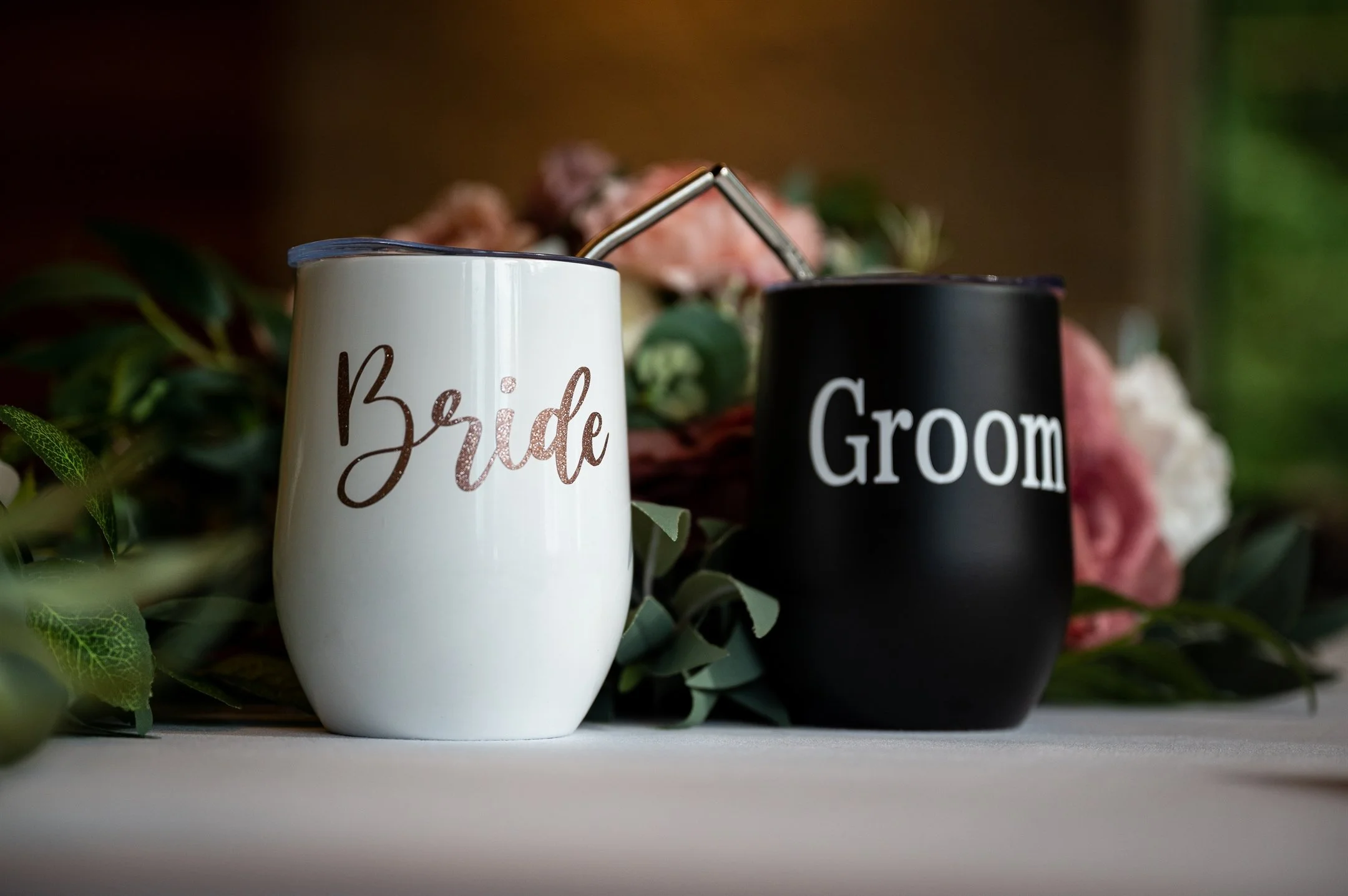 Close-up of bride and groom labeled tumblers on a decorated table.