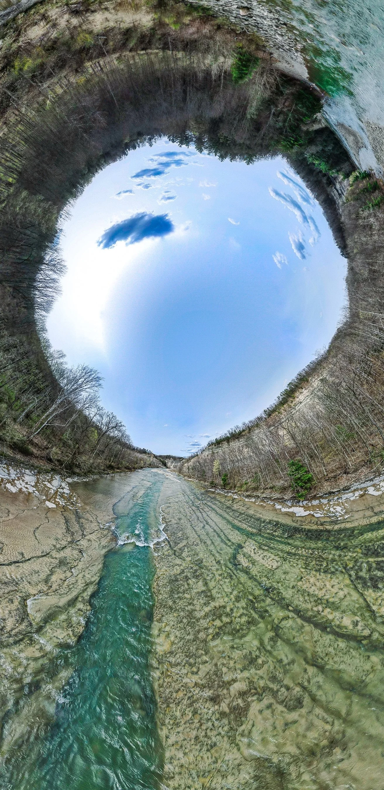 360-degree panoramic view of a river surrounded by trees and hills, blue sky with clouds at the top.