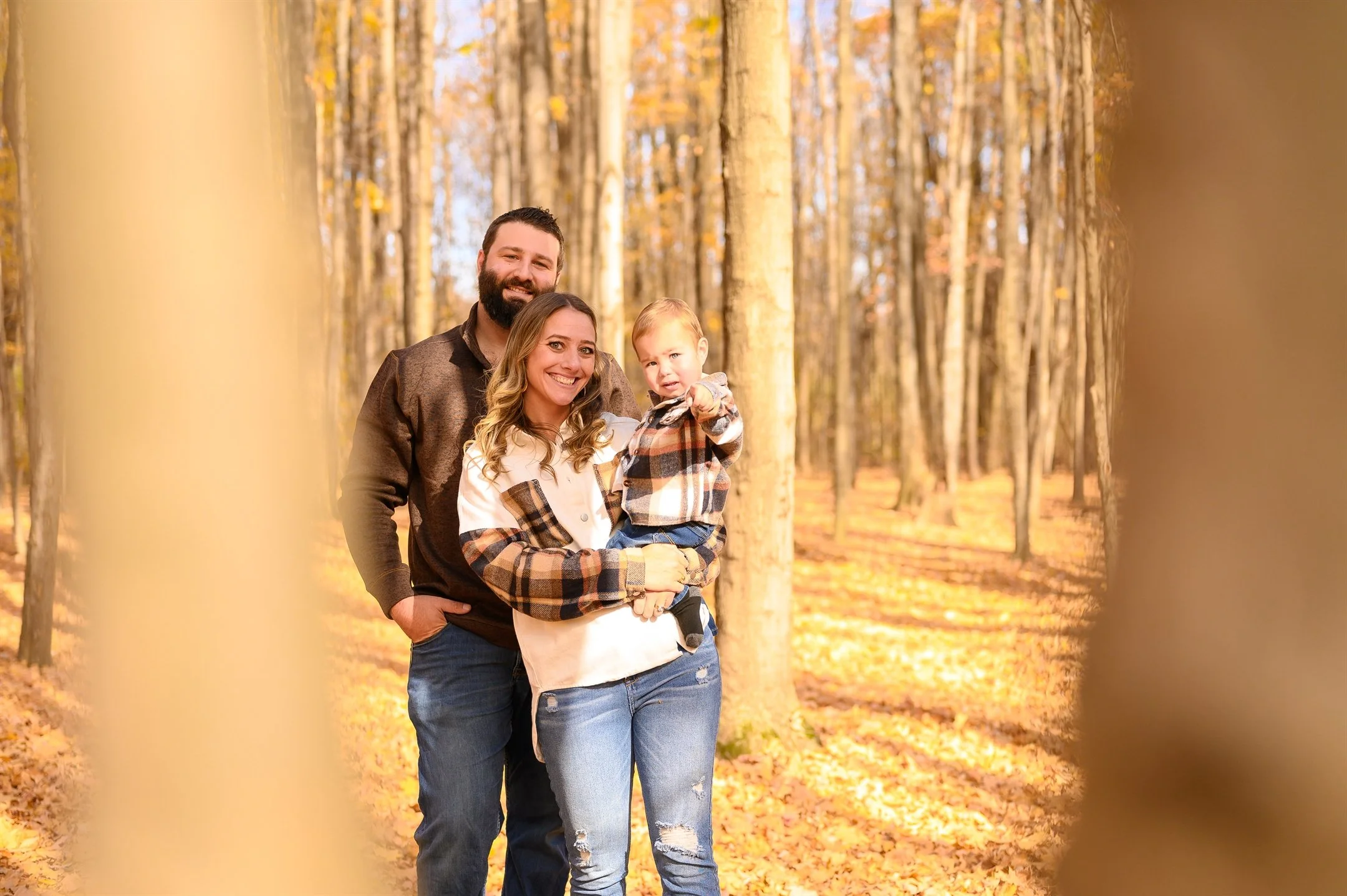 Family of three in a forest during autumn with fallen leaves.