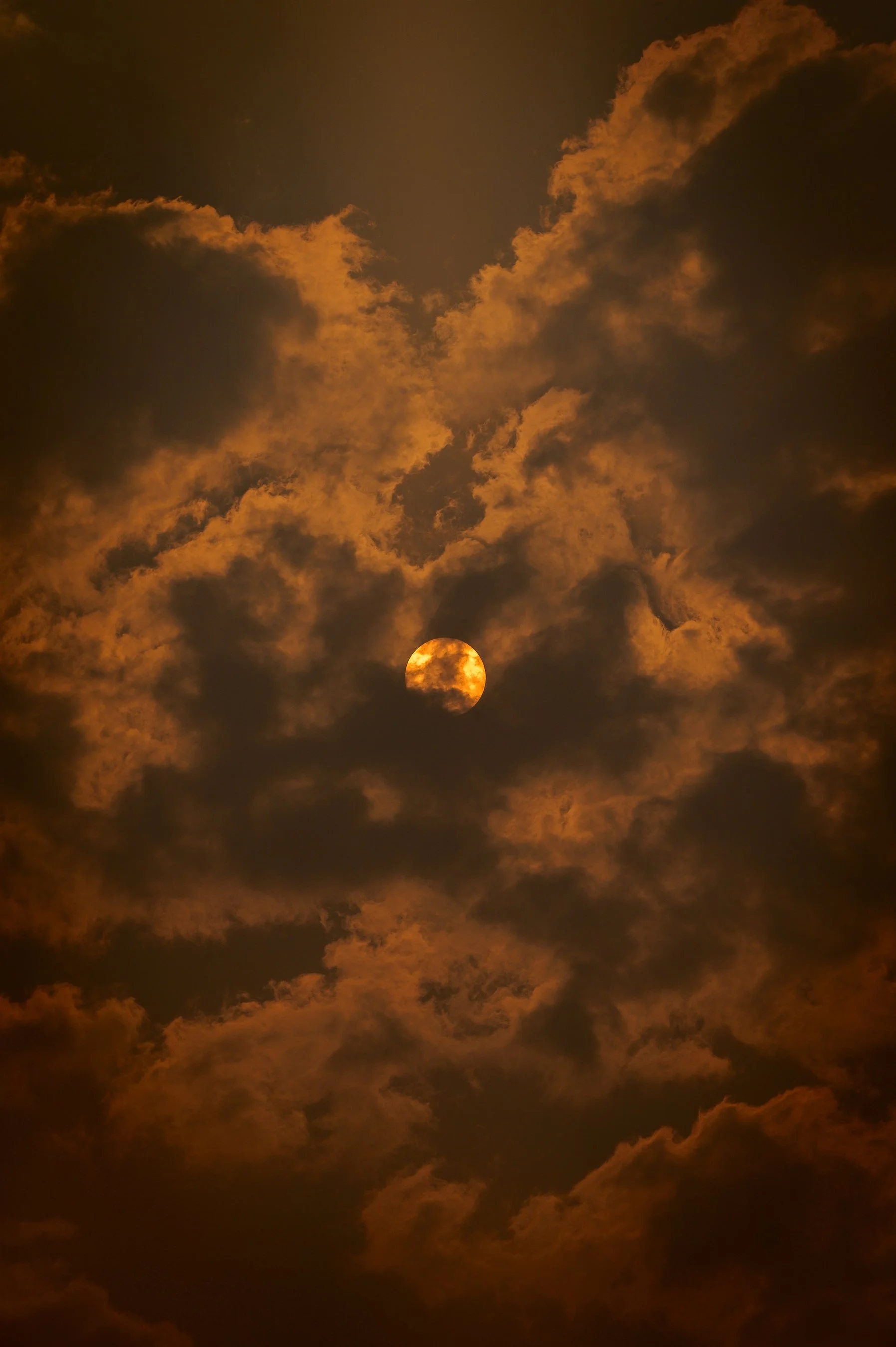 Full moon obscured by dark clouds in an orange-hued night sky.