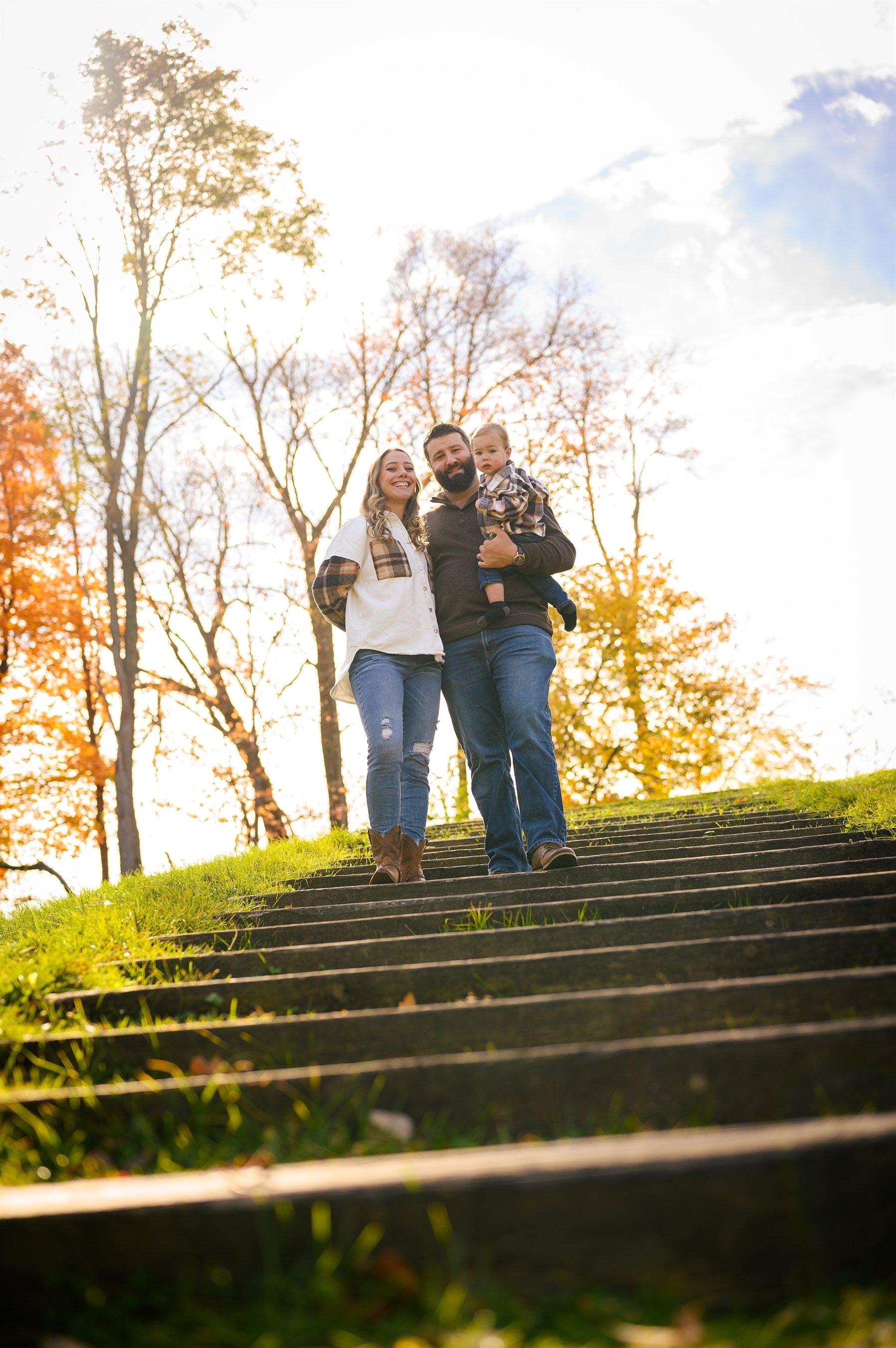 Family standing outdoors on a staircase, surrounded by autumn trees.