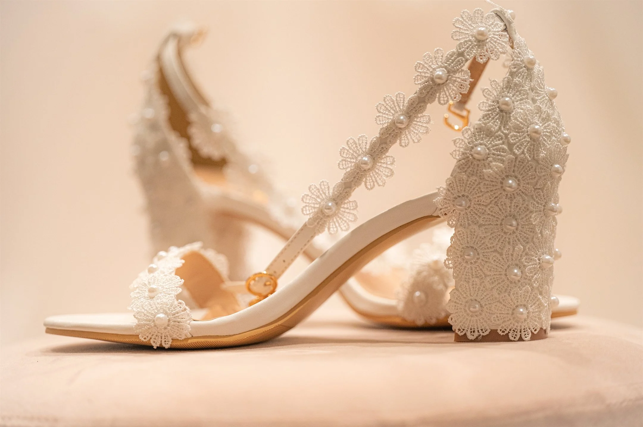 Pair of elegant white high-heel shoes adorned with lace flowers and pearl embellishments.