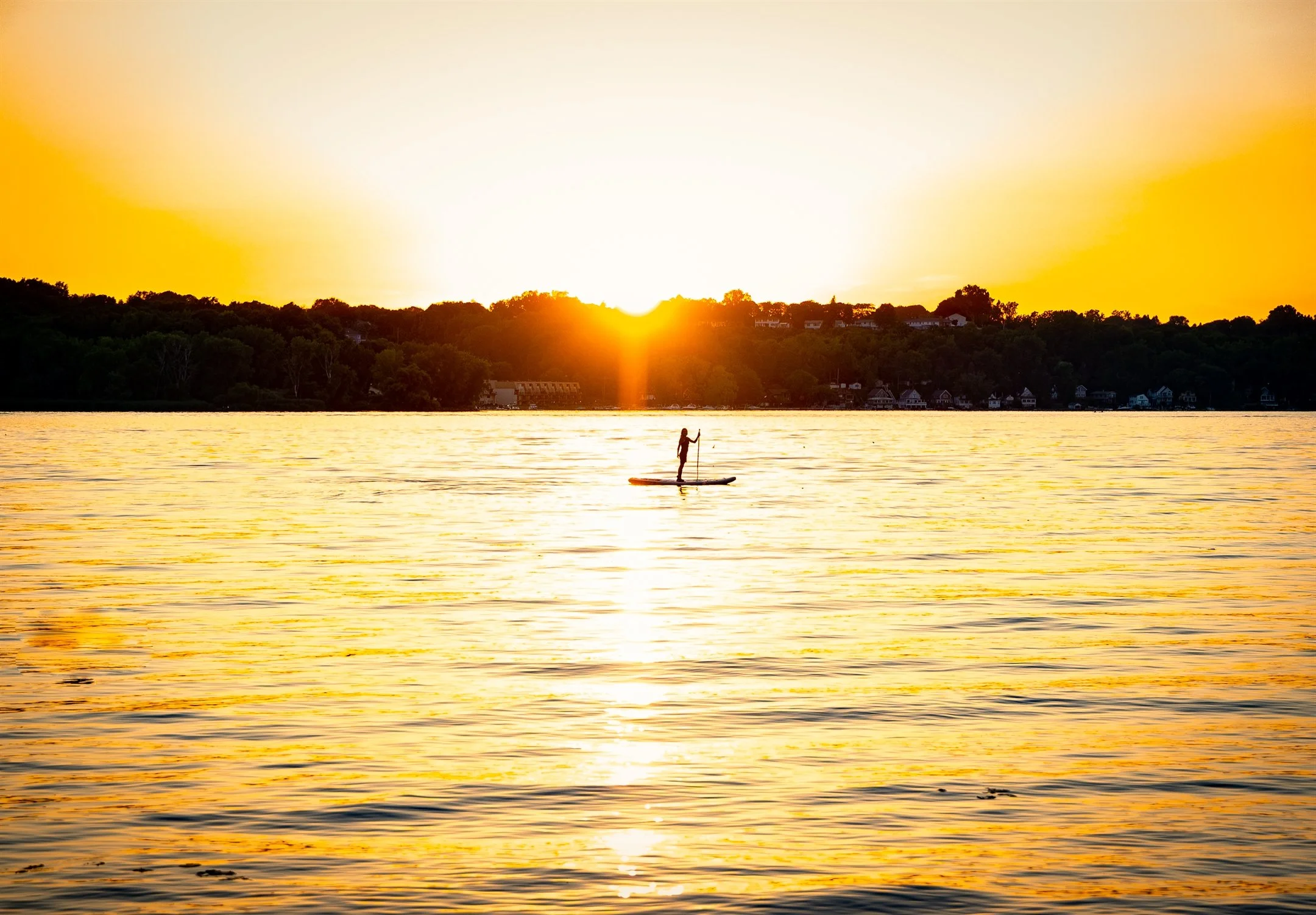 Person paddleboarding on a lake during sunset, with golden light reflecting on the water.