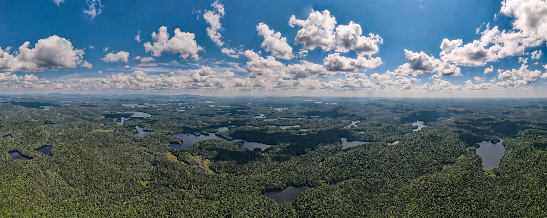 Aerial view of a vast forested landscape with multiple lakes under a partly cloudy sky.