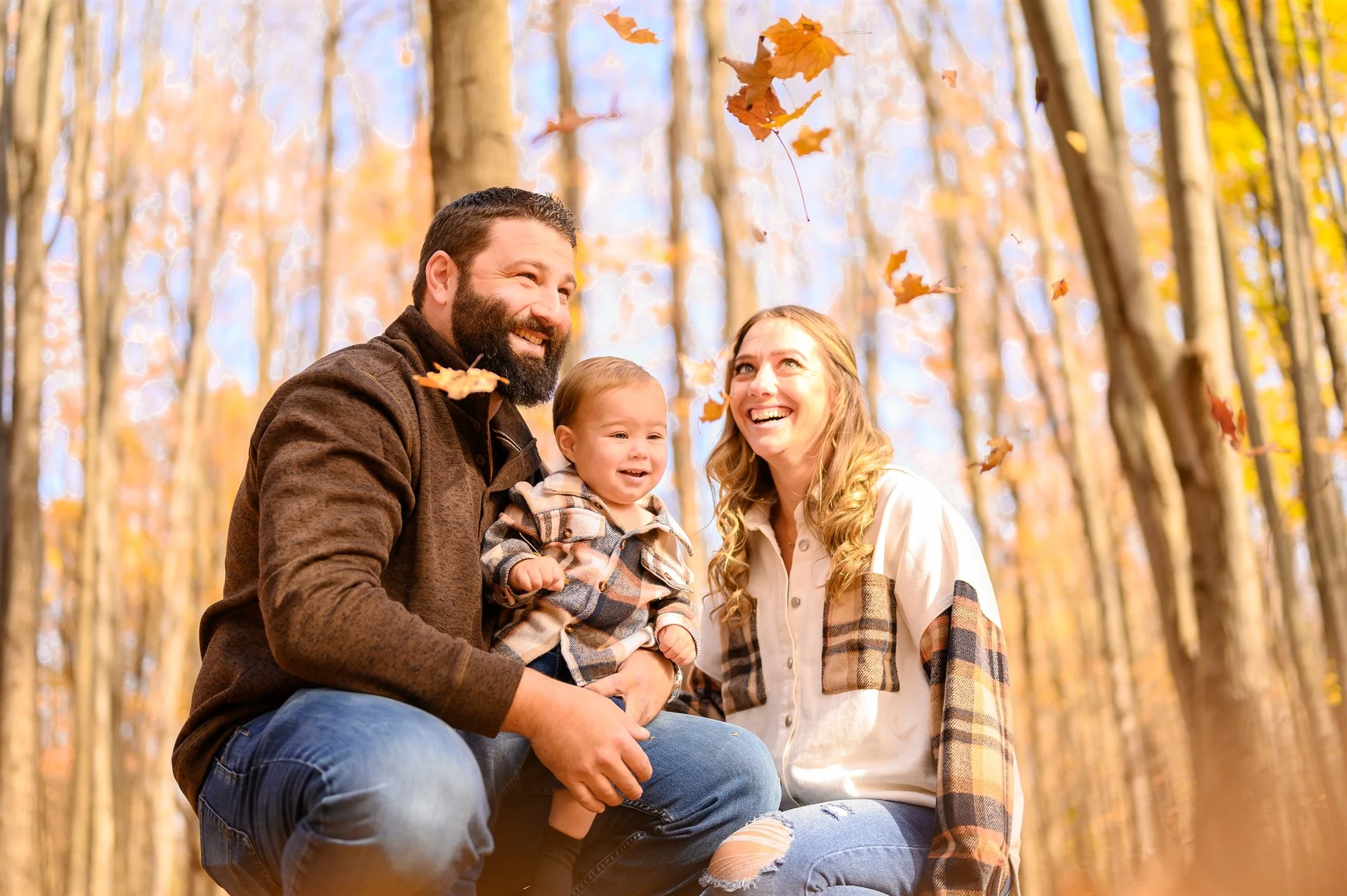Family enjoying autumn in a forest with falling leaves.
