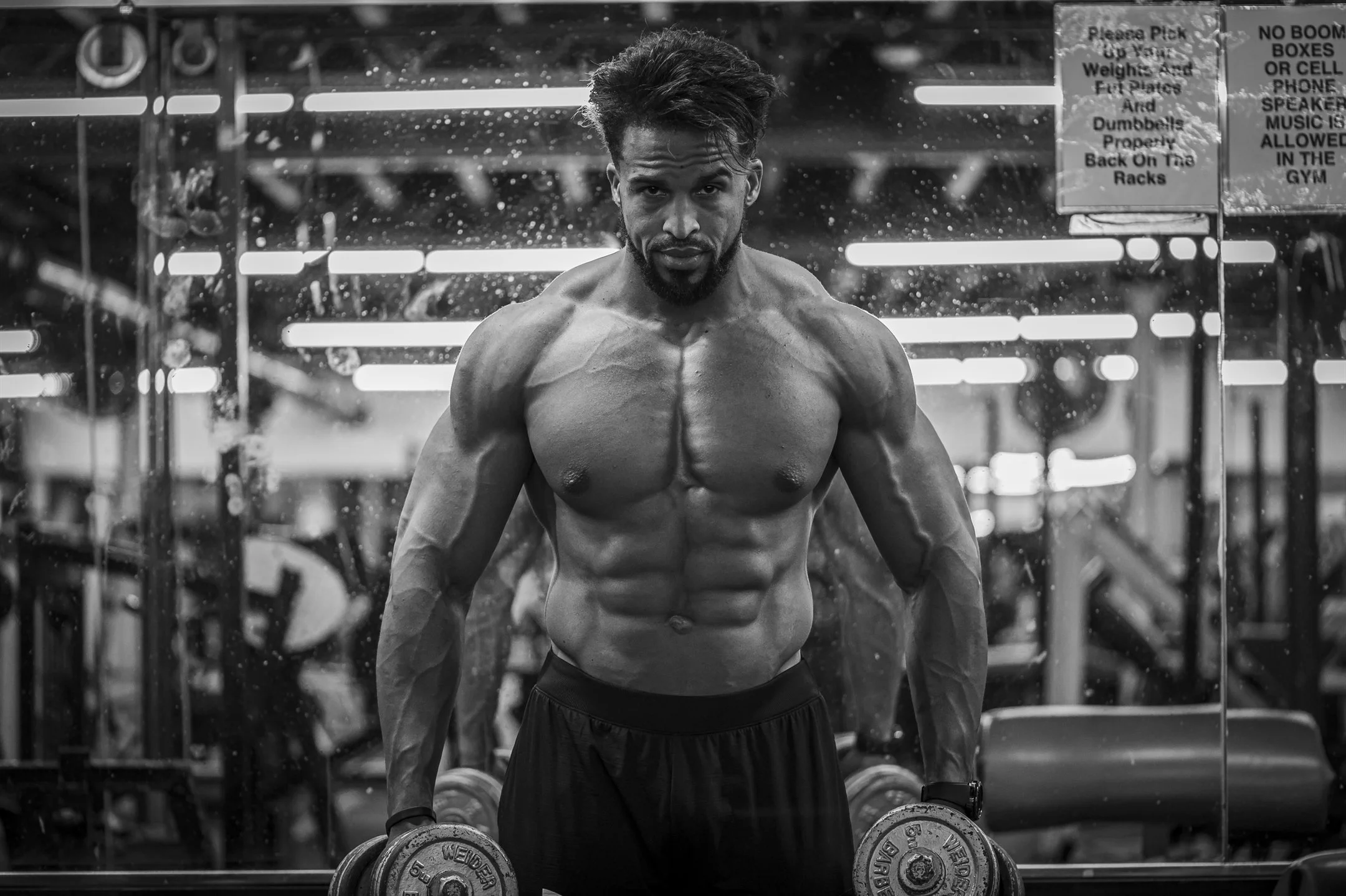 Muscular man lifting dumbbells in a gym, black and white photo