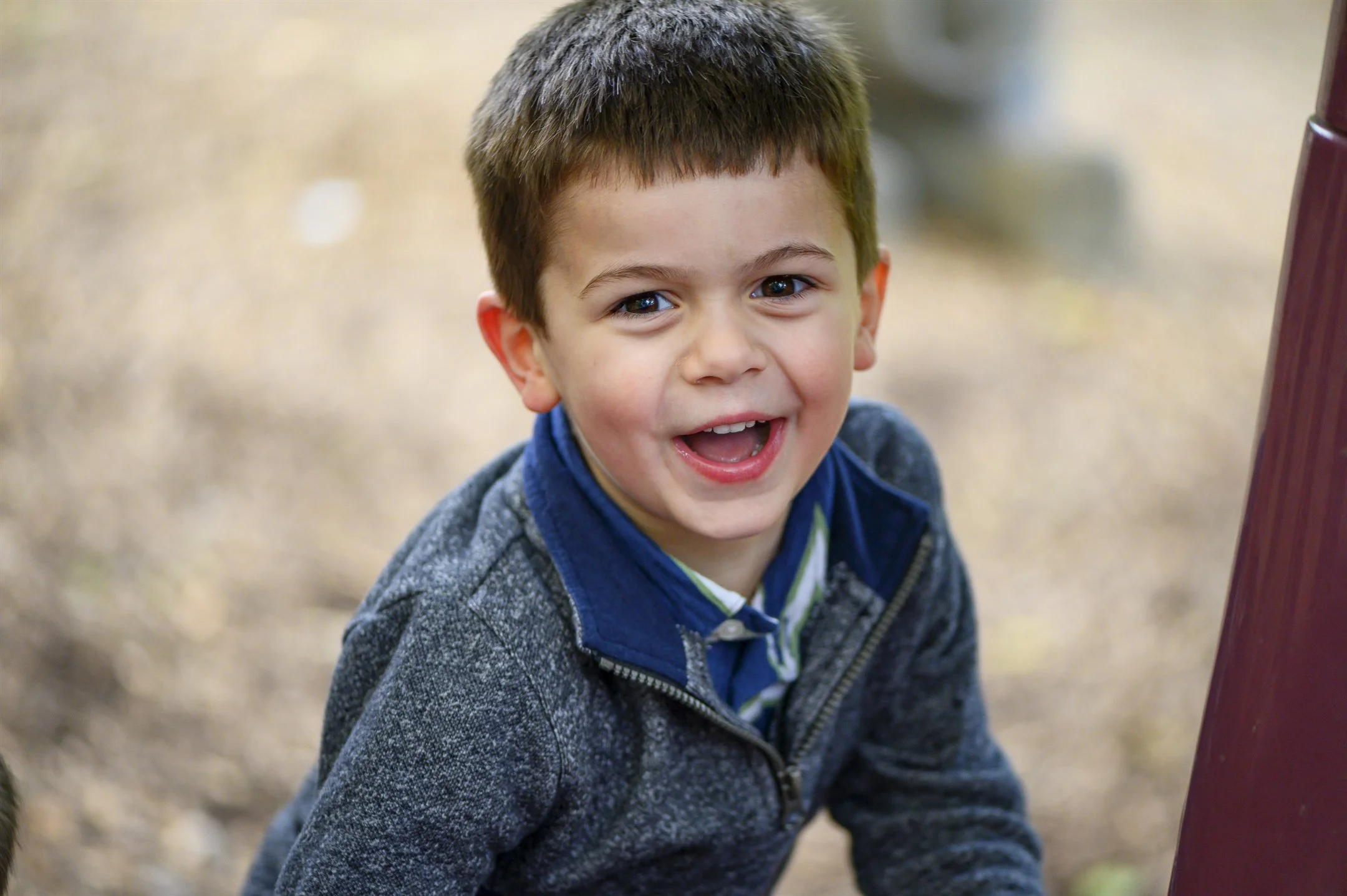 A smiling child in a gray jacket outdoors.